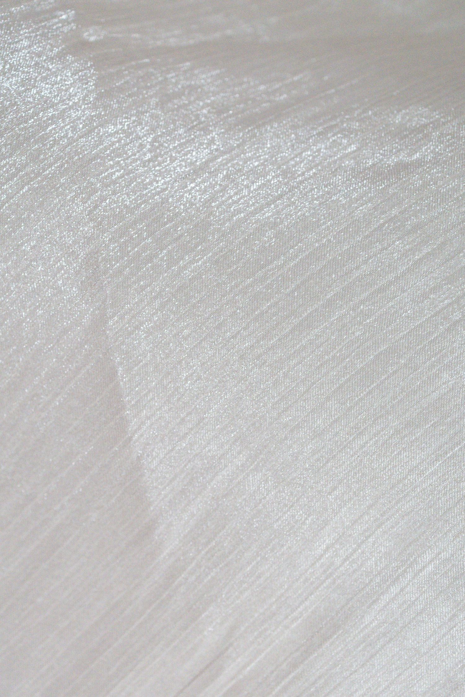 Close-up of shimmering white fabric with subtle texture and soft light reflections creating an elegant, luxurious appearance.