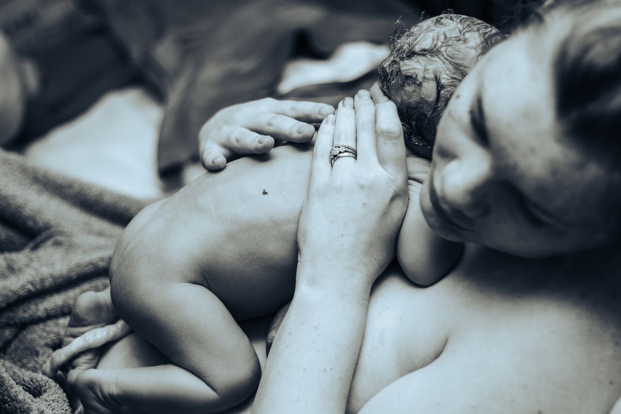 Black and white photo of a mother tenderly holding and kissing her newborn baby while lying down.