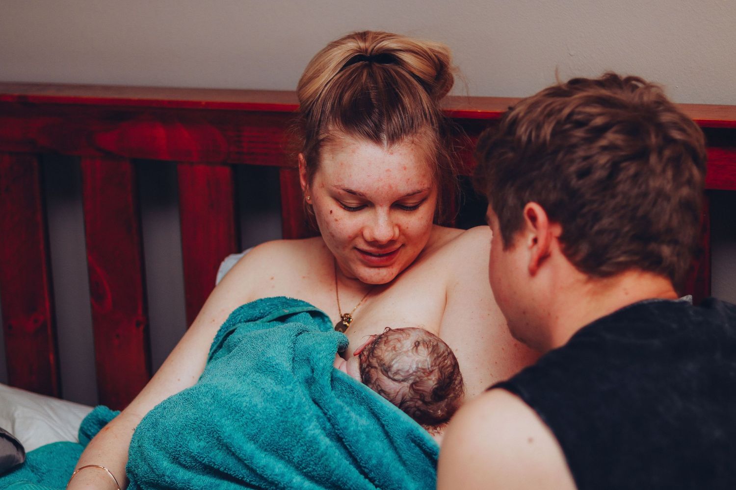 New mother gazing lovingly at her newborn while partner looks on during home birth.