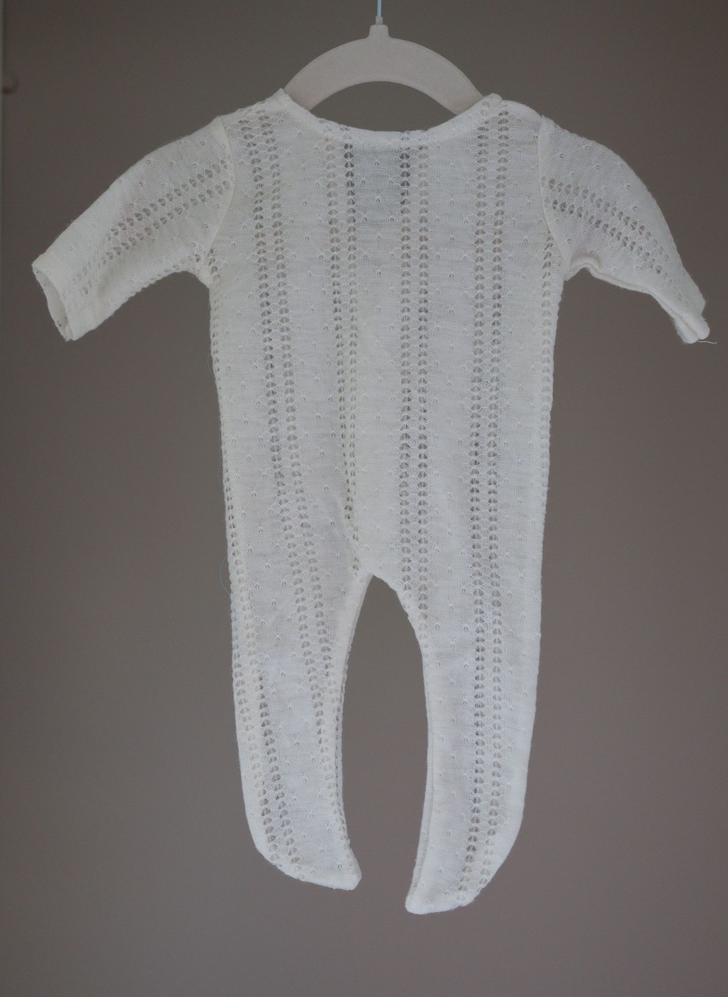White knitted baby footie Pjs onesie with open-weave pattern, displayed on hanger against gray background. Taken by Golden Hour Perth
