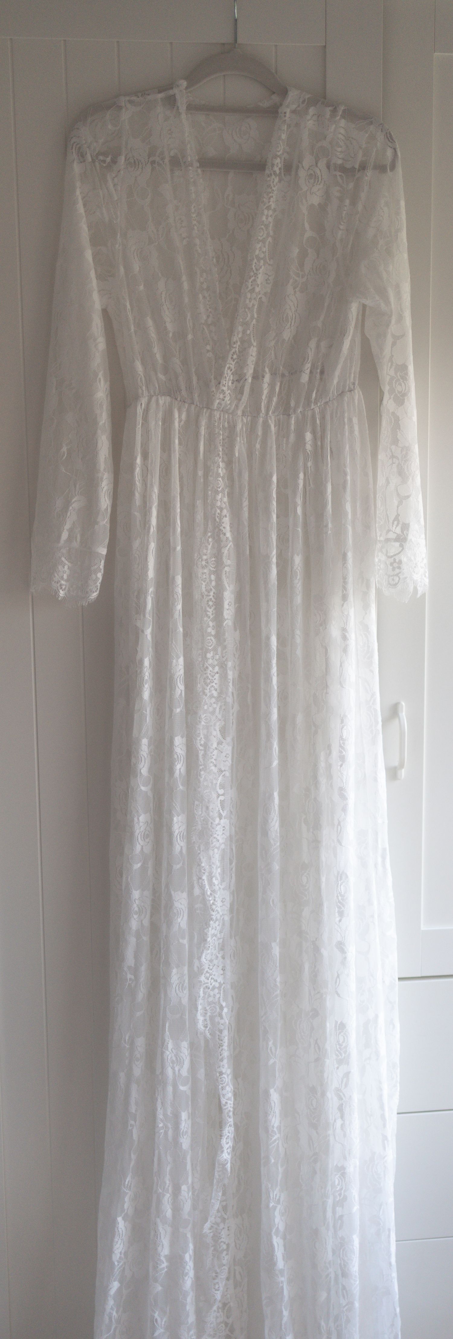 White lace maxi dress with long sleeves and deep V-neckline, hanging on a door hanger.