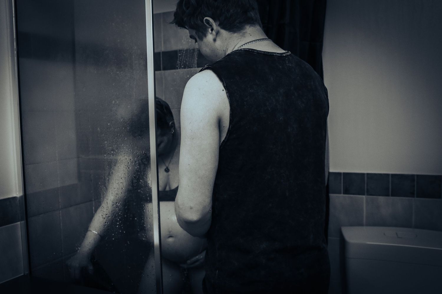 Adult and child standing near a glass shower door in a dimly lit bathroom.