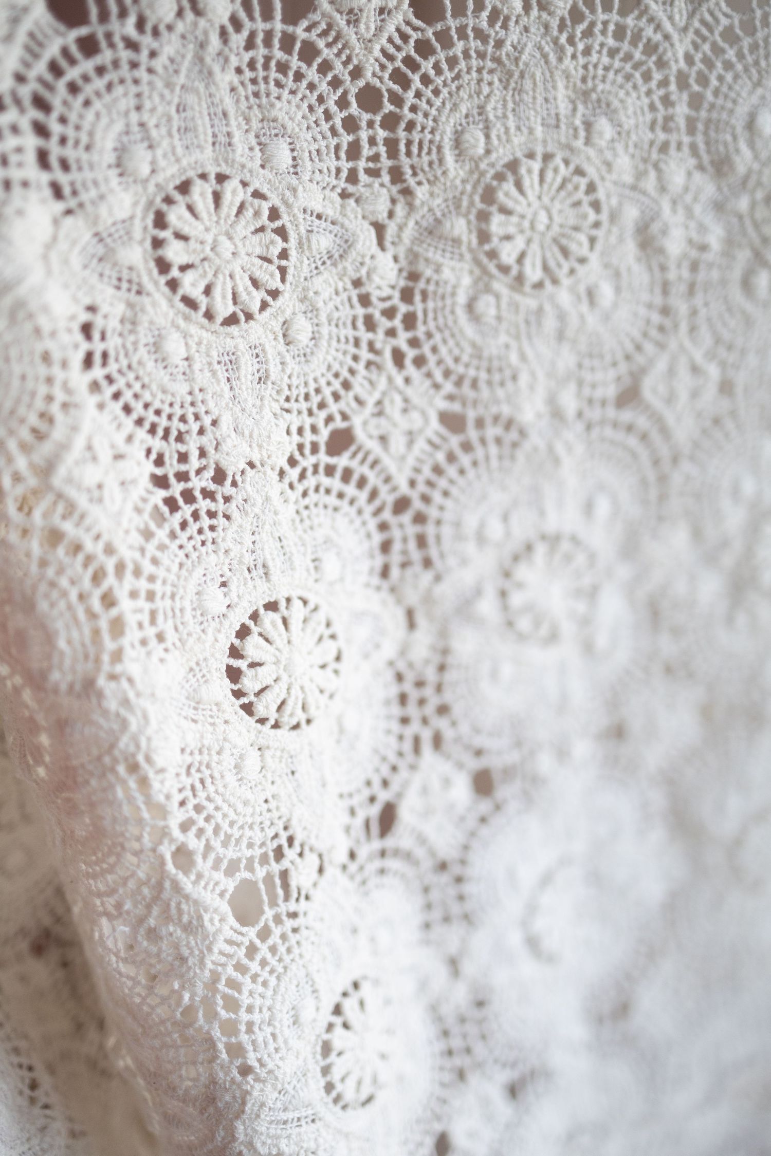 Close-up of delicate white crochet lace fabric featuring intricate circular floral patterns, ideal for bridal or vintage fashion.
