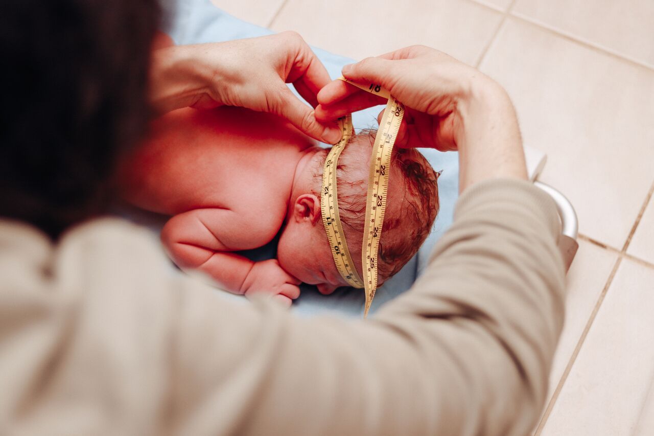 Healthcare professional measuring newborn baby head circumference with yellow tape measure after birth.