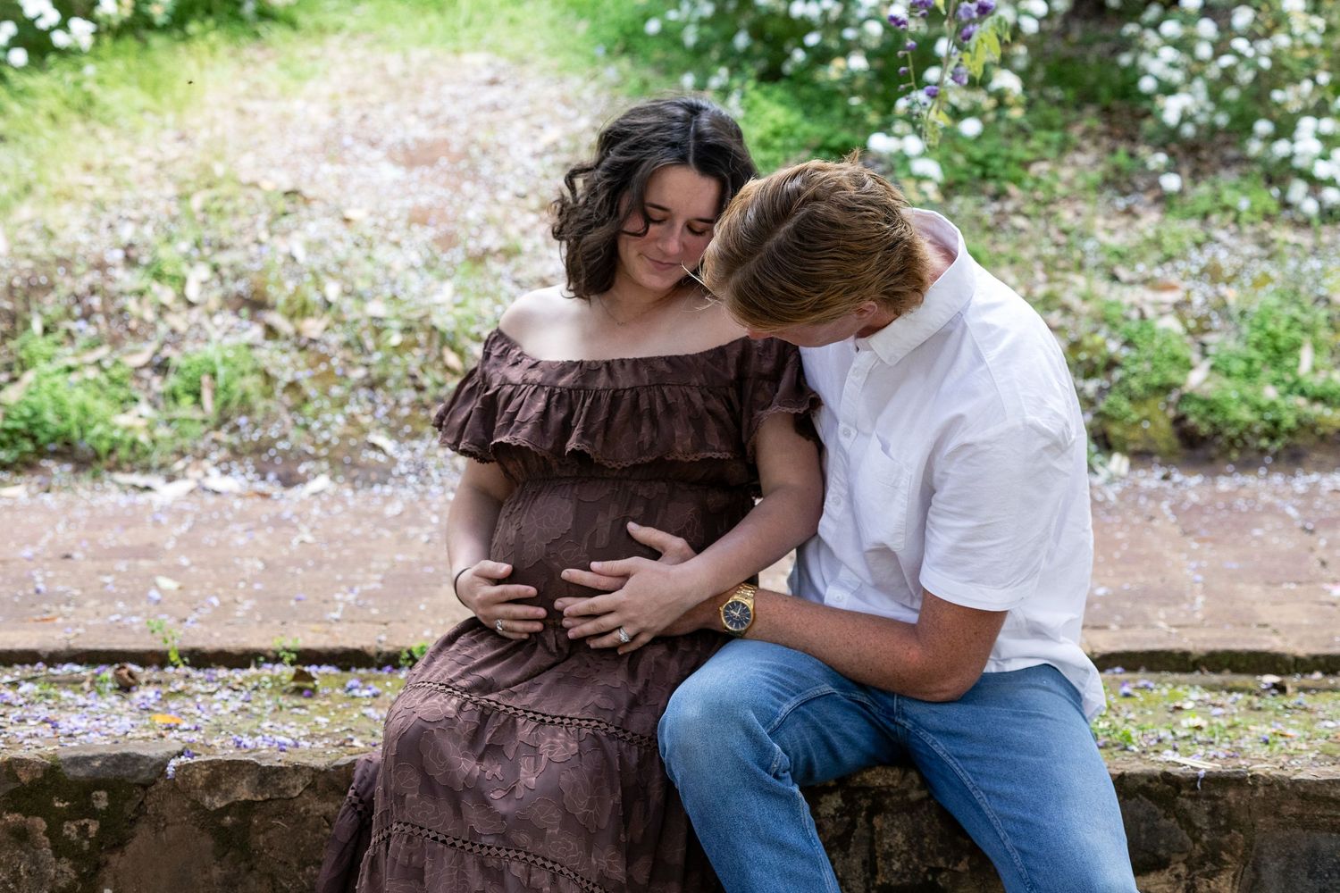 Couple sharing a tender moment during maternity photo session outdoors, woman in brown dress cradling baby bump.  Araluen Perth