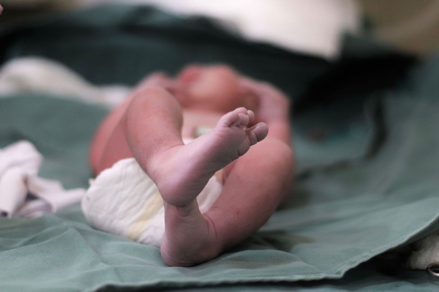 Close-up of a newborn baby's feet and legs on a green medical cloth.