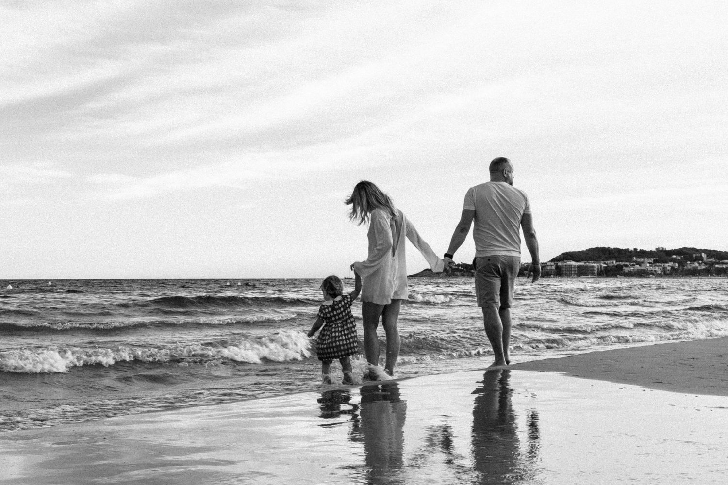 Black and white photo of family with young child walking along ocean shoreline.