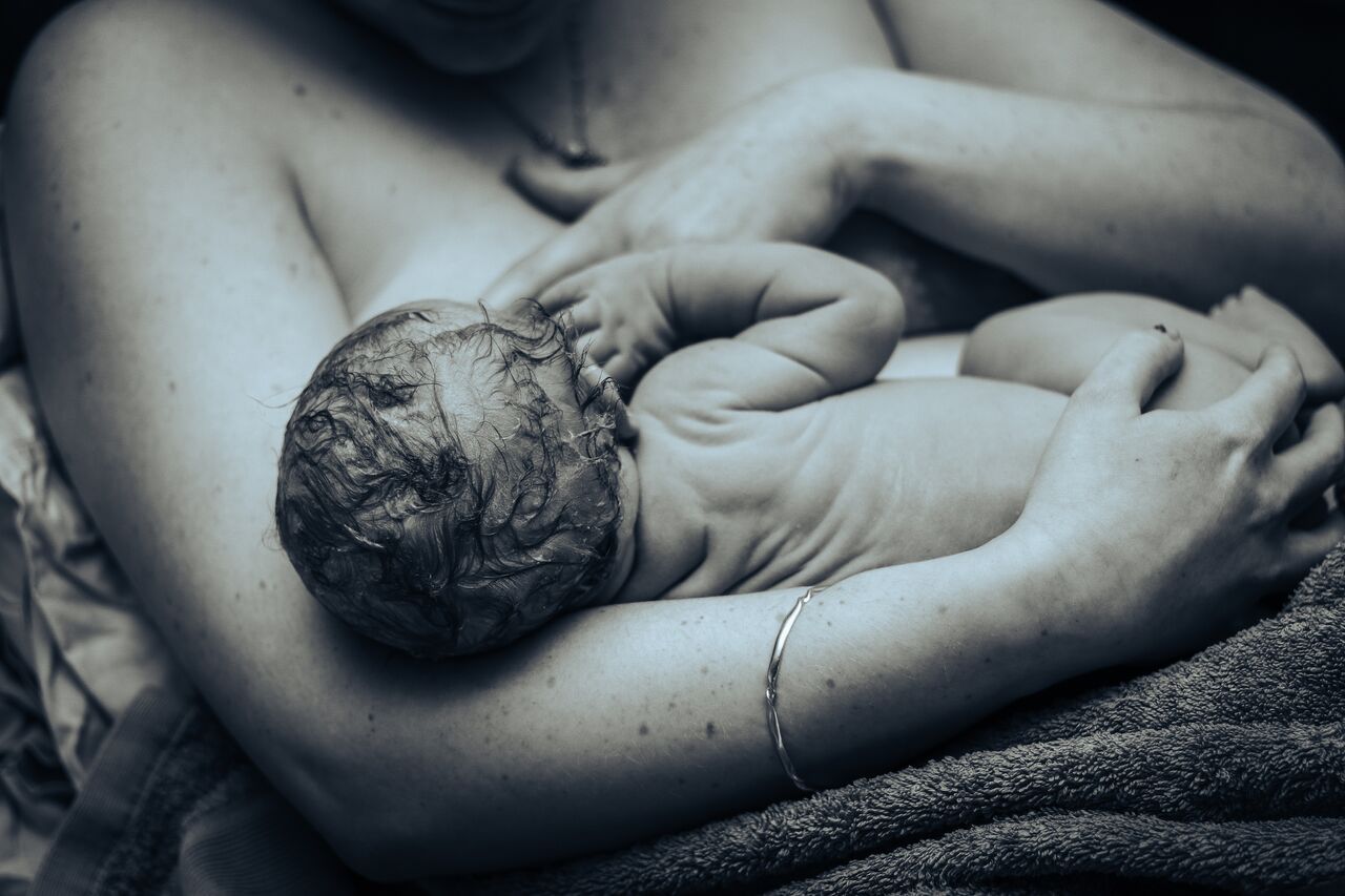 Black and white photo of a newborn baby being held skin-to-skin by mother immediately after birth.