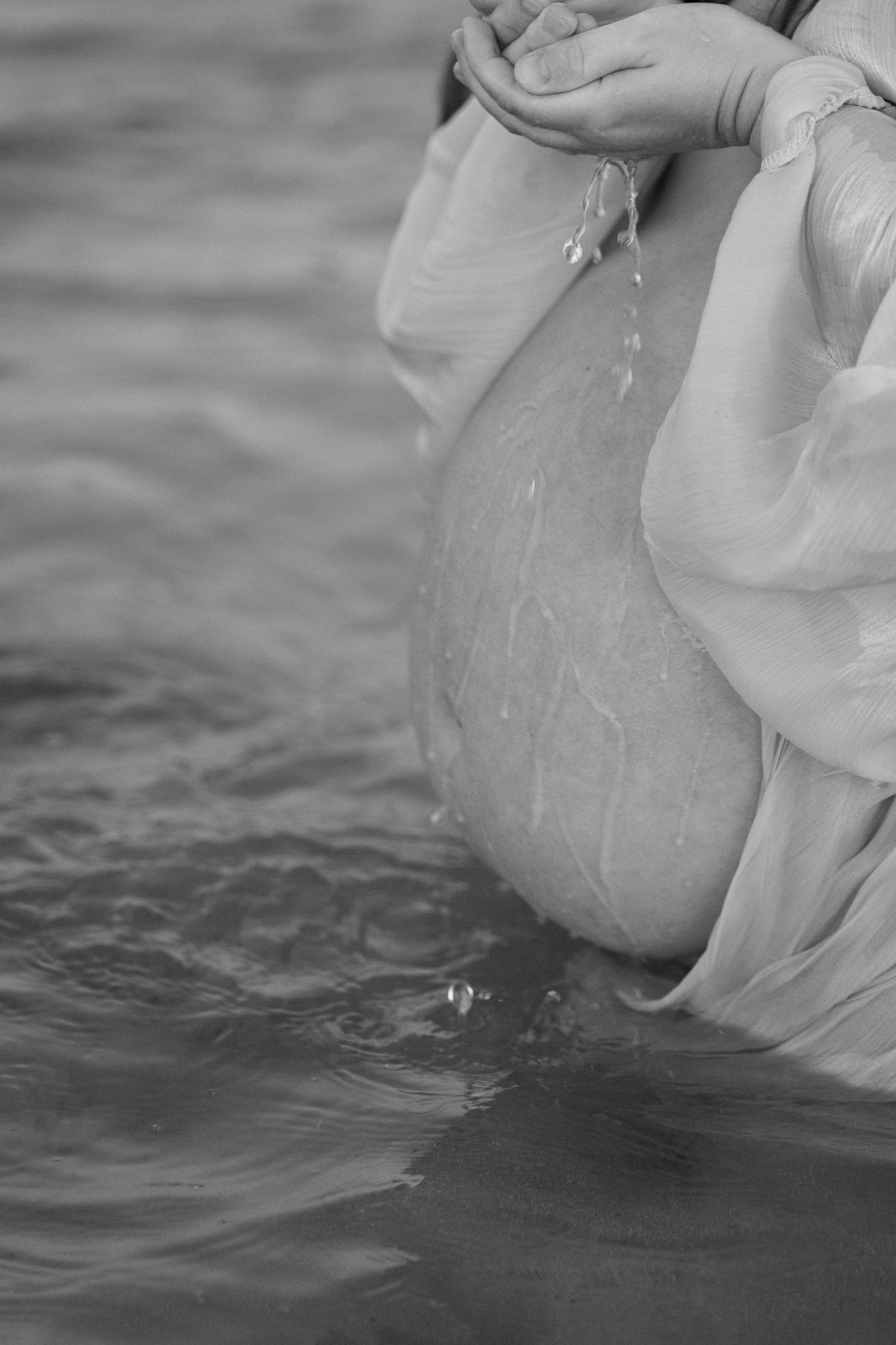 Black and white close-up of pregnant belly with water droplets falling from hands in ocean. Woodman Point Perth