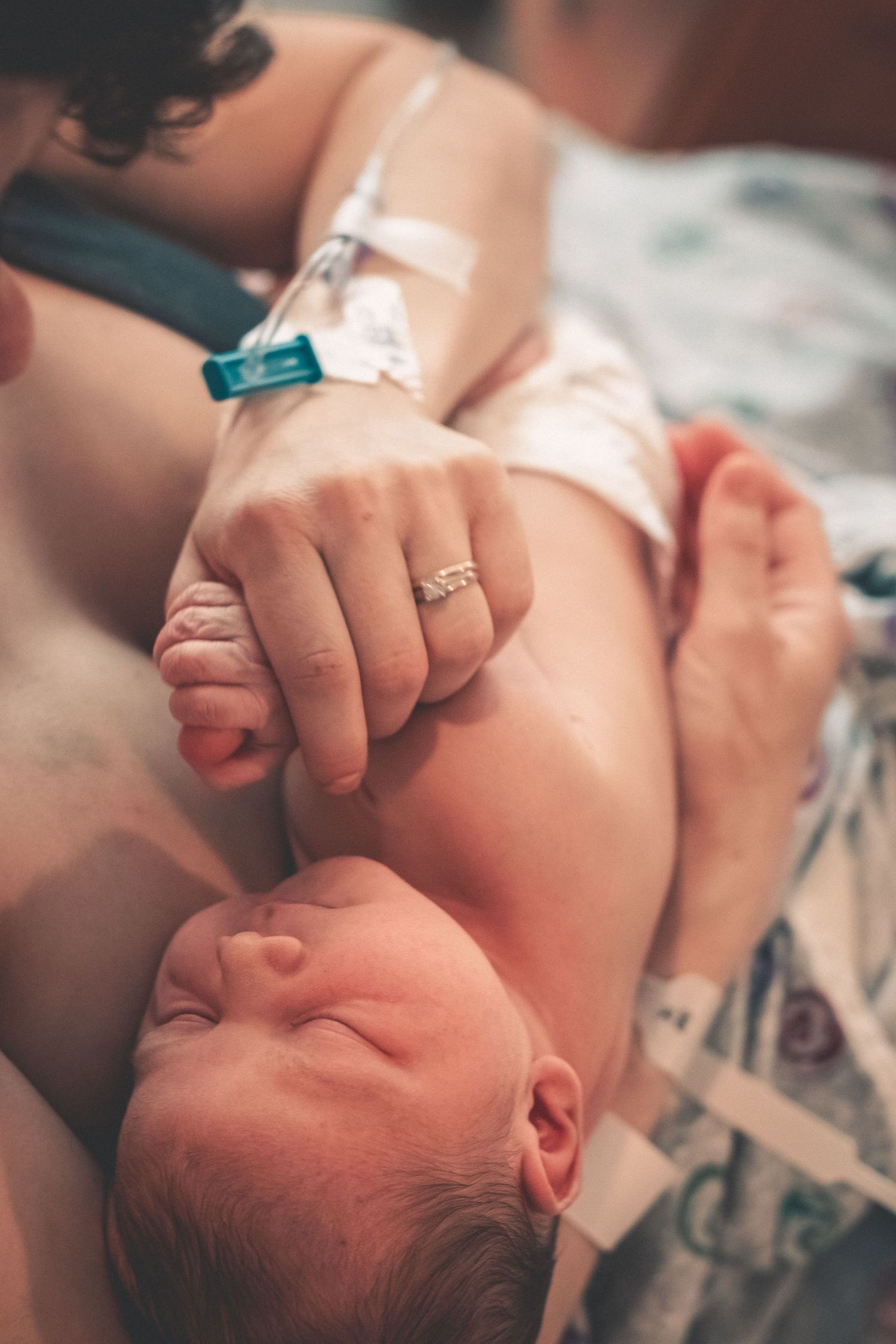 Newborn baby grasping mother's finger in hospital bed during first moments after birth.