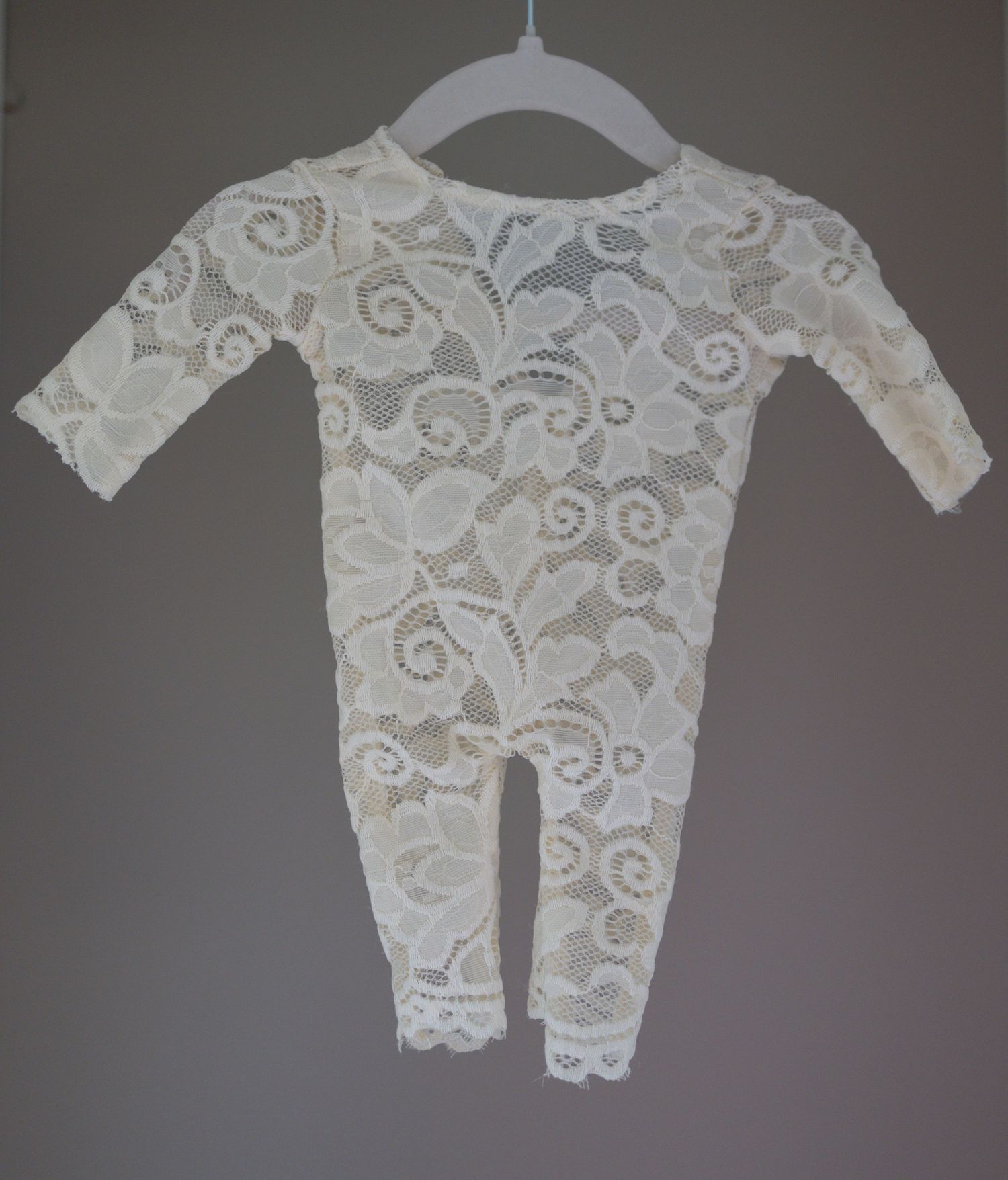 Ivory cream lace baby romper with long sleeves and floral pattern, displayed on hanger against gray background. Taken by Golden Hour Perth