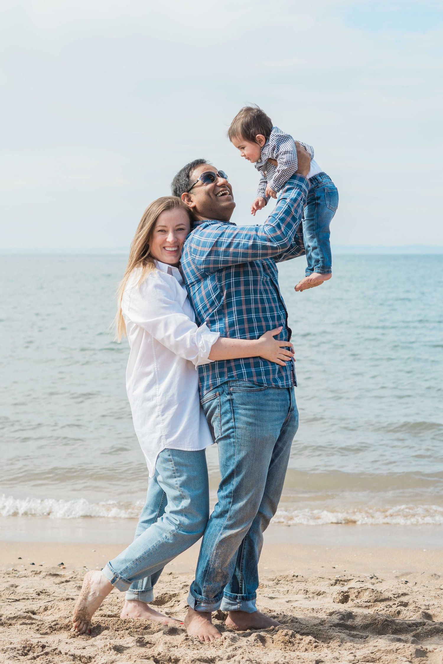 Joyful interracial family with baby enjoying a sunny beach day together.