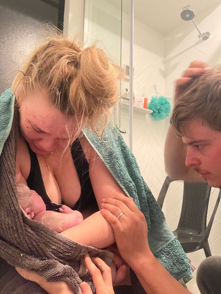 Emotional new mother holding her newborn in a bathroom with partner beside her.