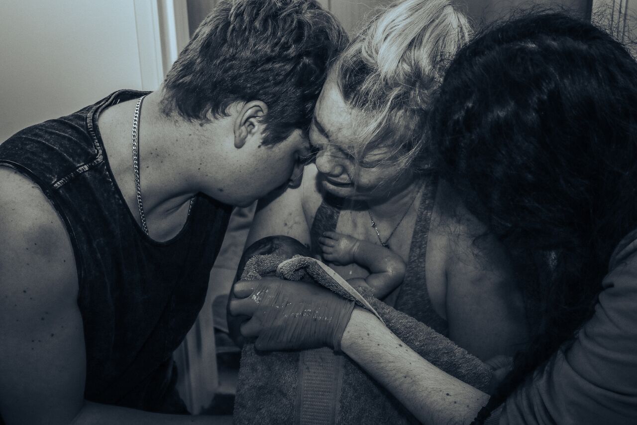 Black and white birth photo of a mother supported by her partner and doula during active labor.