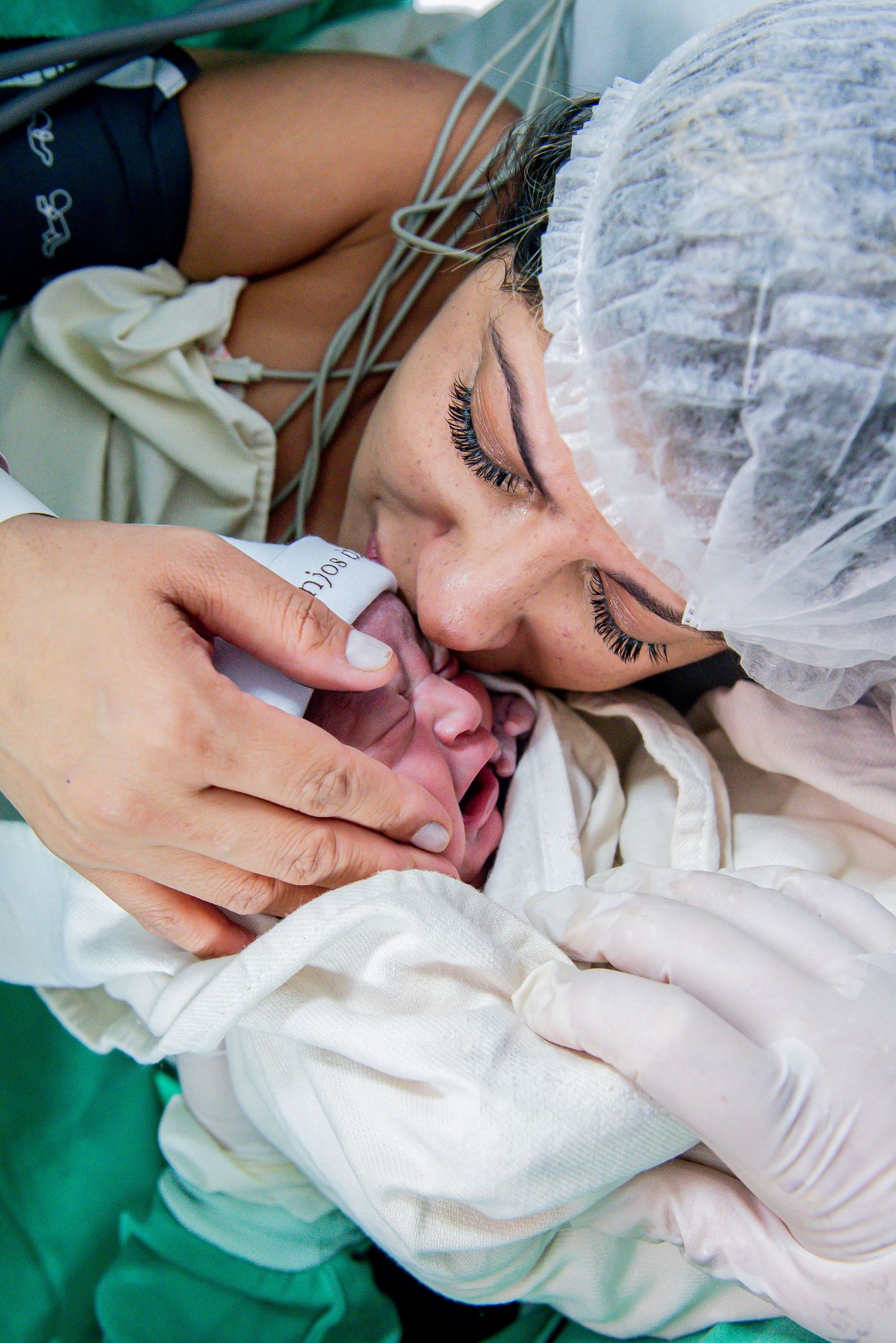 Emotional mother in surgical cap kissing her crying newborn baby after cesarean section delivery.