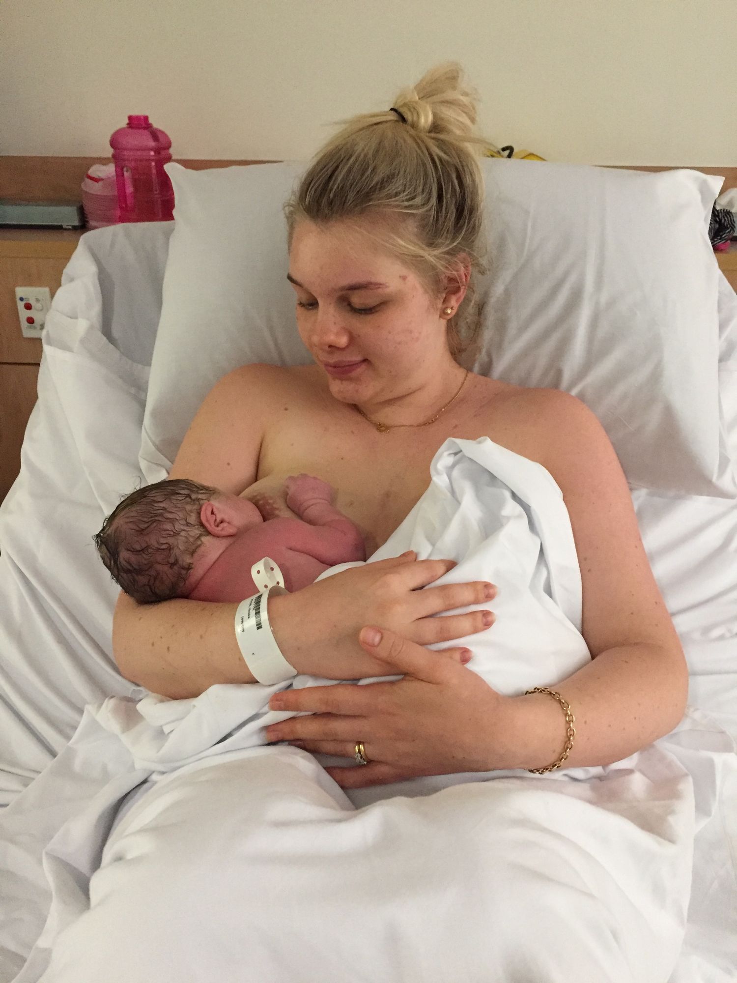 Blonde mother in hospital bed holding her newborn baby skin-to-skin after delivery.