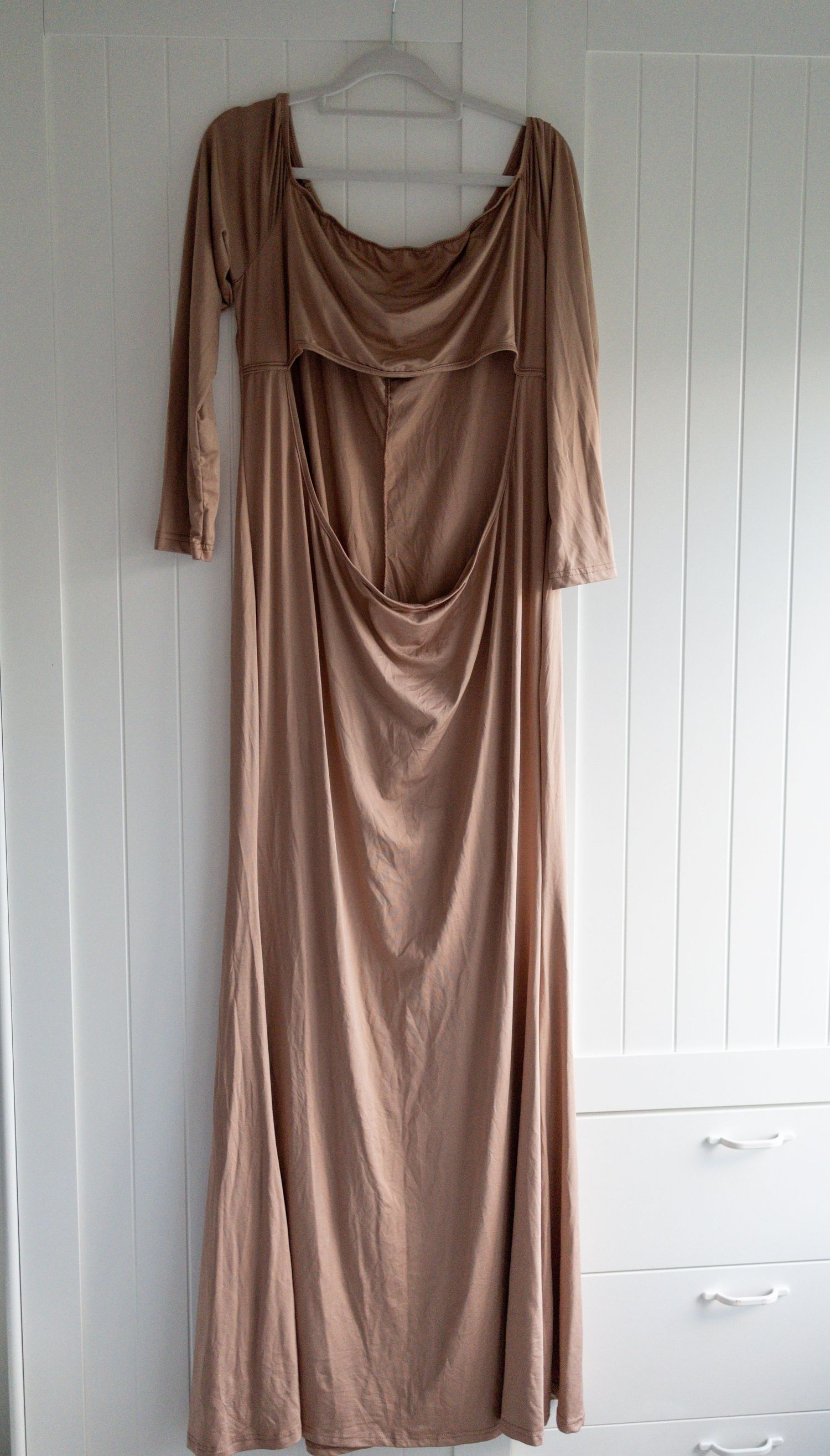 Elegant long-sleeve maxi dress in champagne gold satin with draped cowl neckline, hanging on white wall.
