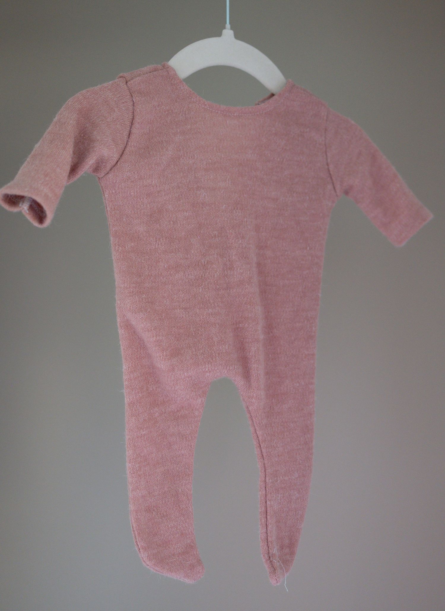 Pink marl knit baby footed sleepsuit onesie displayed on a white hanger against a grey background. Taken by Golden Hour Perth