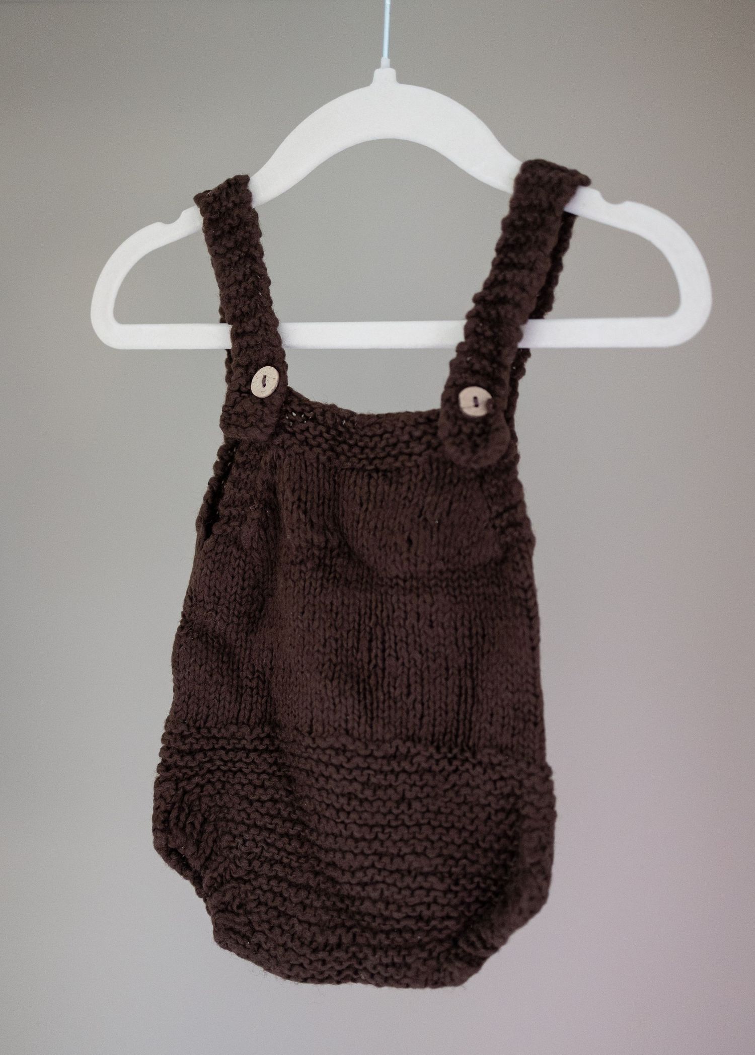 Brown knitted baby romper with button straps hanging on a white hanger. Taken by Golden Hour Perth