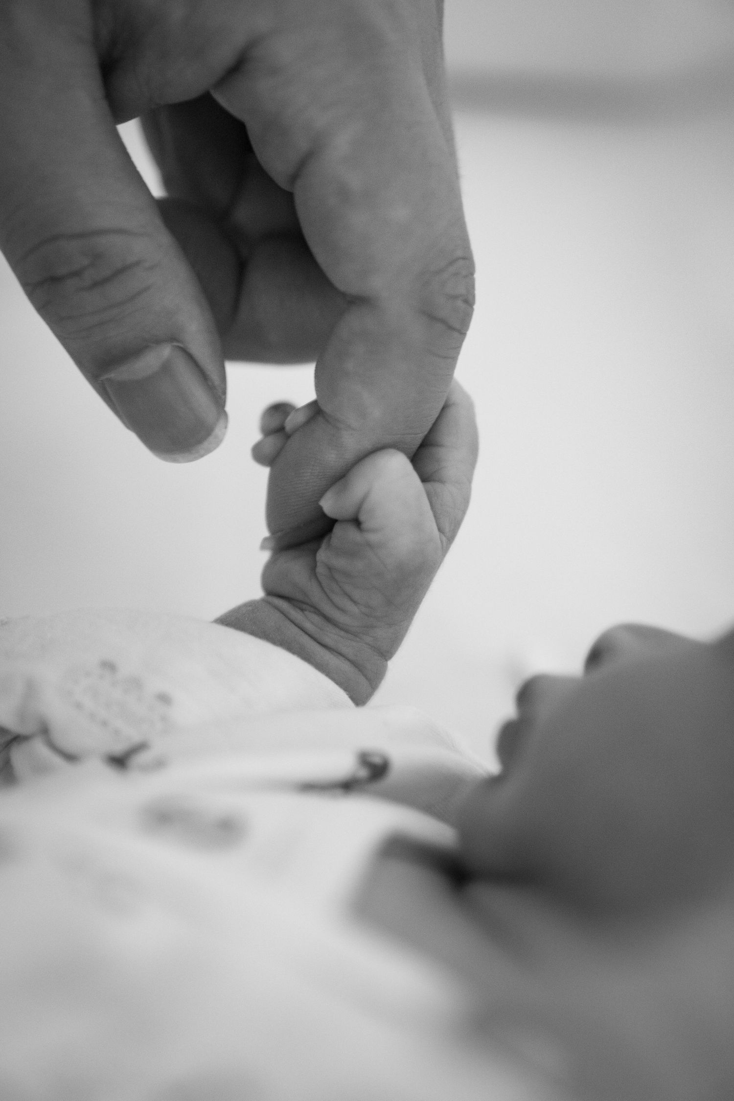 Close-up black and white photo of an adult finger being grasped by a tiny newborn baby hand.