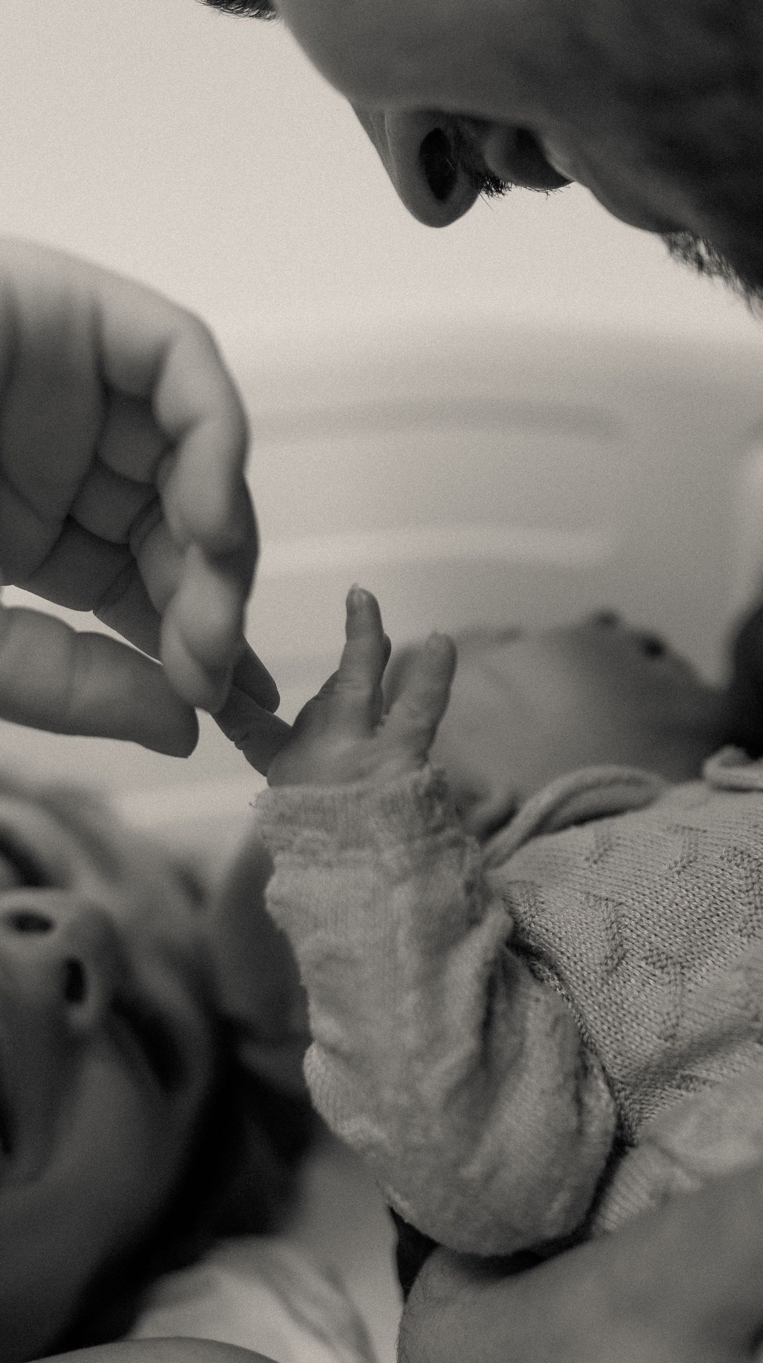 Black and white photo of a newborn baby grasping an adult finger, capturing a tender parent-child bonding moment.