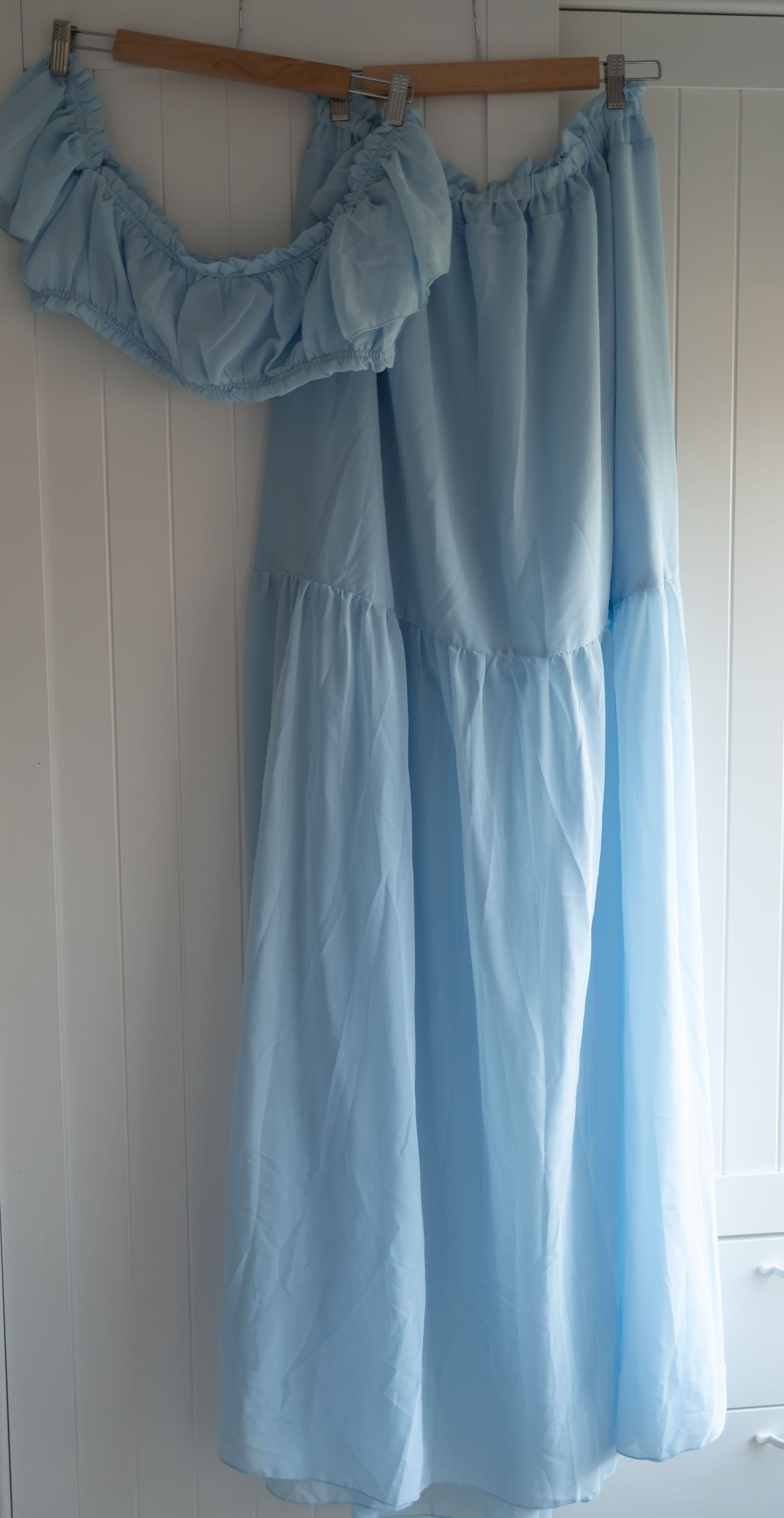 Light blue off-shoulder maxi dress with ruffled neckline and tiered skirt, hanging on a wooden hanger.