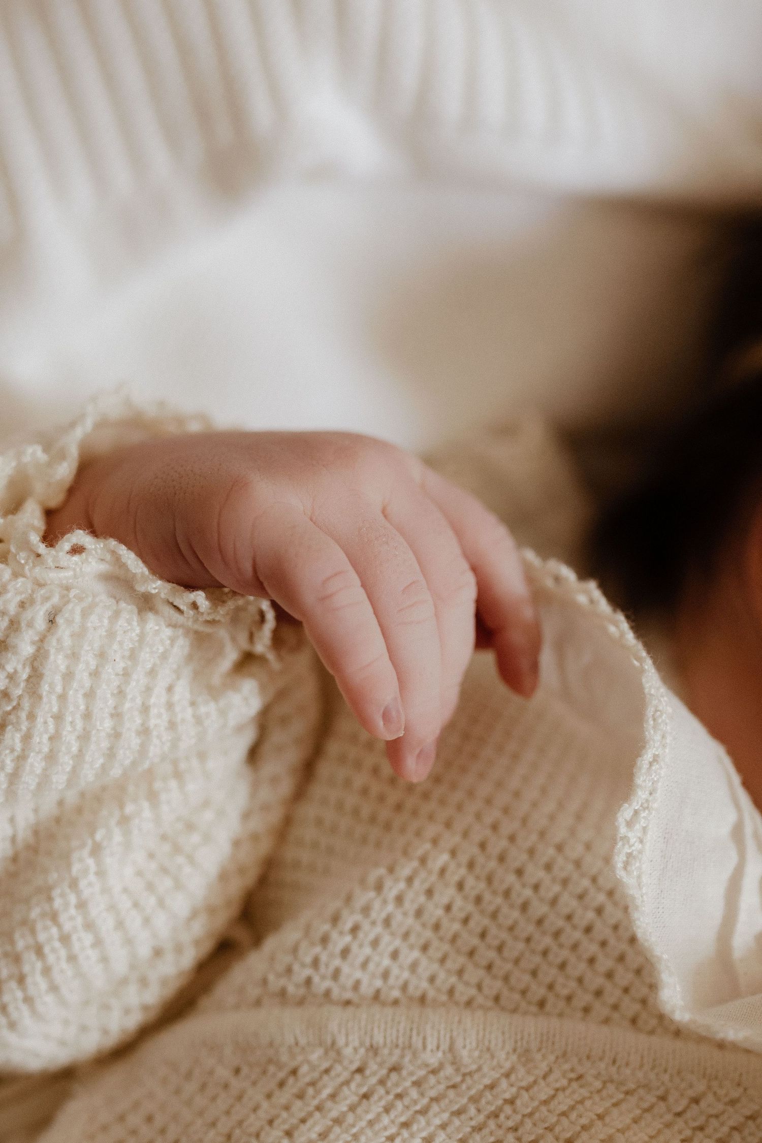 Close-up of a newborn baby's tiny hand resting on a cream knit blanket with delicate lace trim.