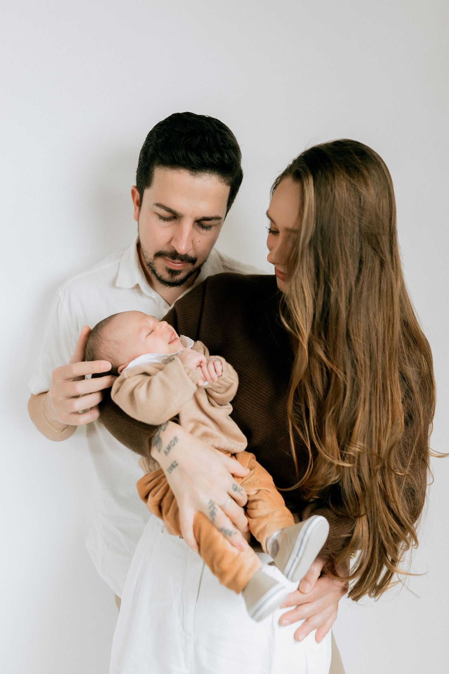 Young parents lovingly looking at their newborn baby against a white studio background.