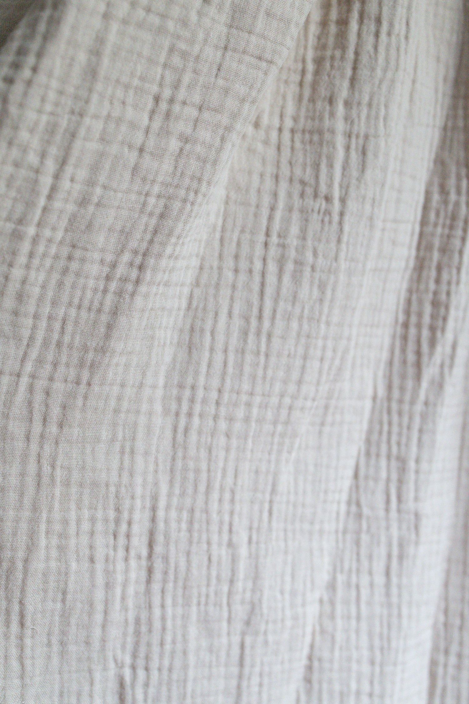 Close-up of soft white crinkled muslin fabric with a delicate woven texture and gentle folds.