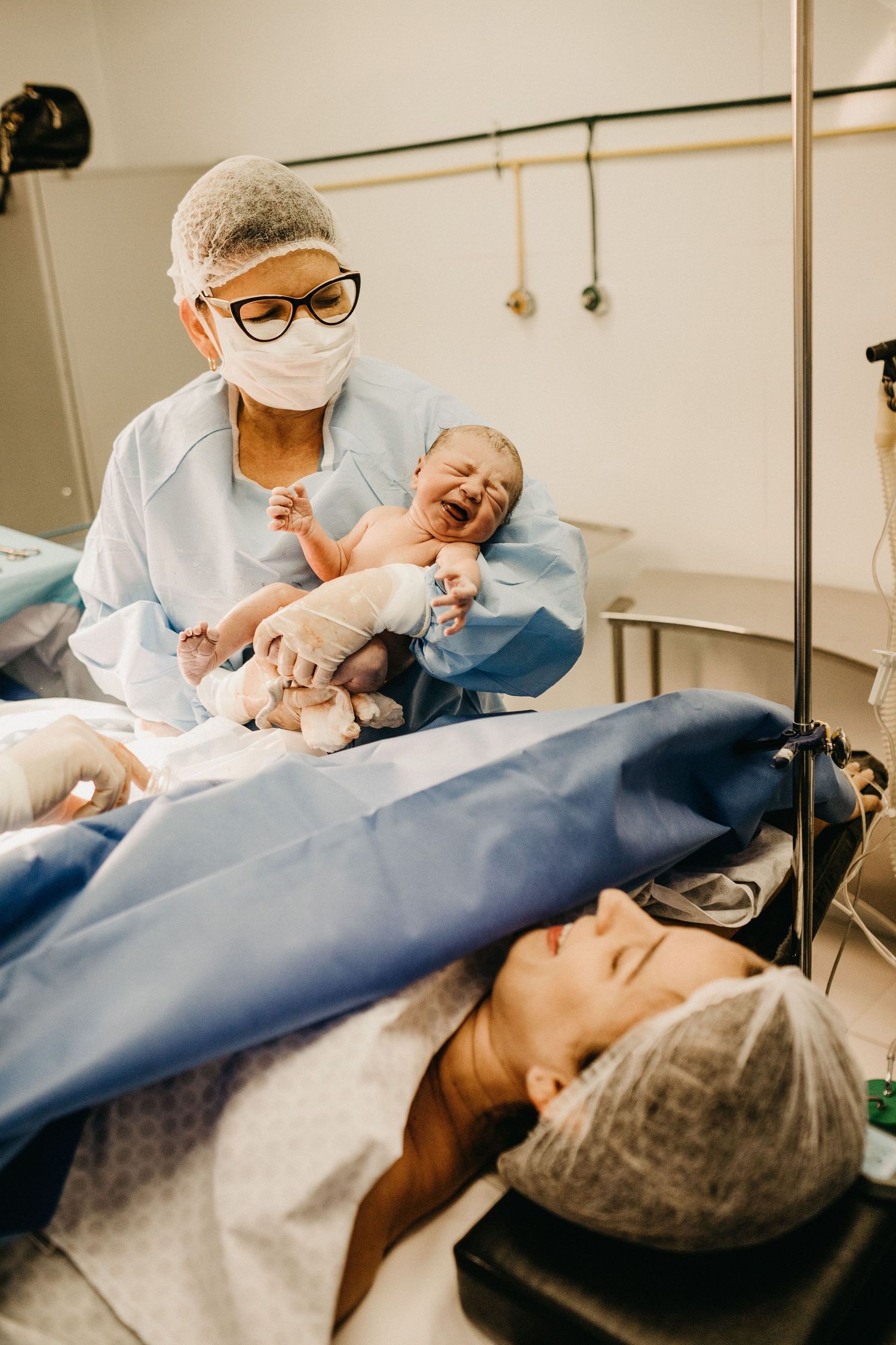 Medical professional in surgical mask presenting crying newborn to mother after C-section delivery.