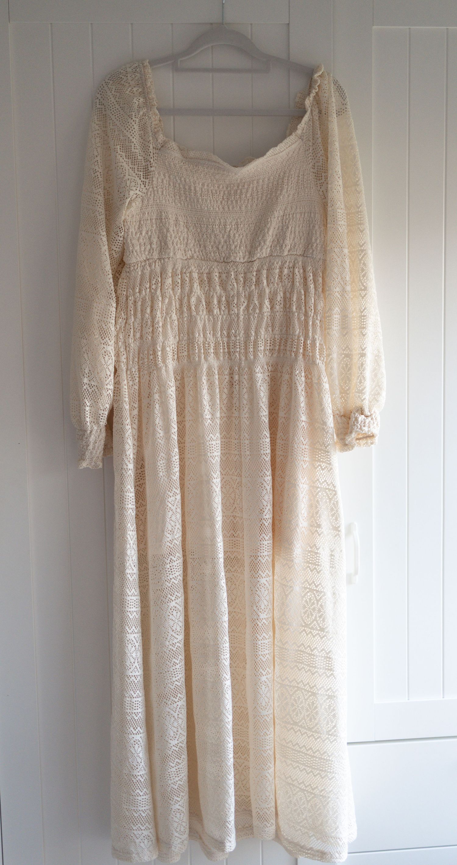 Vintage cream lace maxi dress with long sleeves, smocked bodice, and flowing skirt, displayed on a hanger.