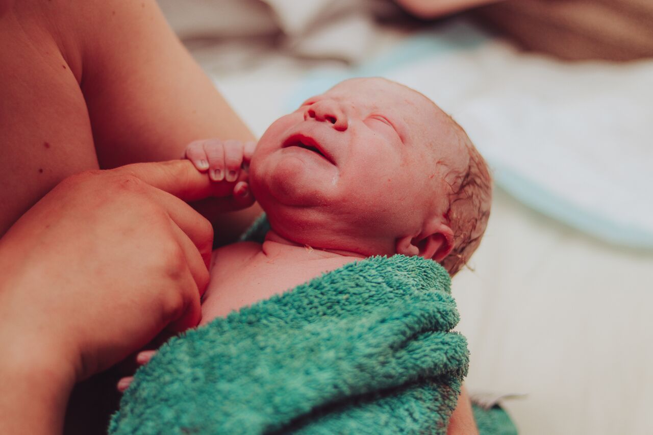 Newborn baby wrapped in teal towel being held by mother after birth.