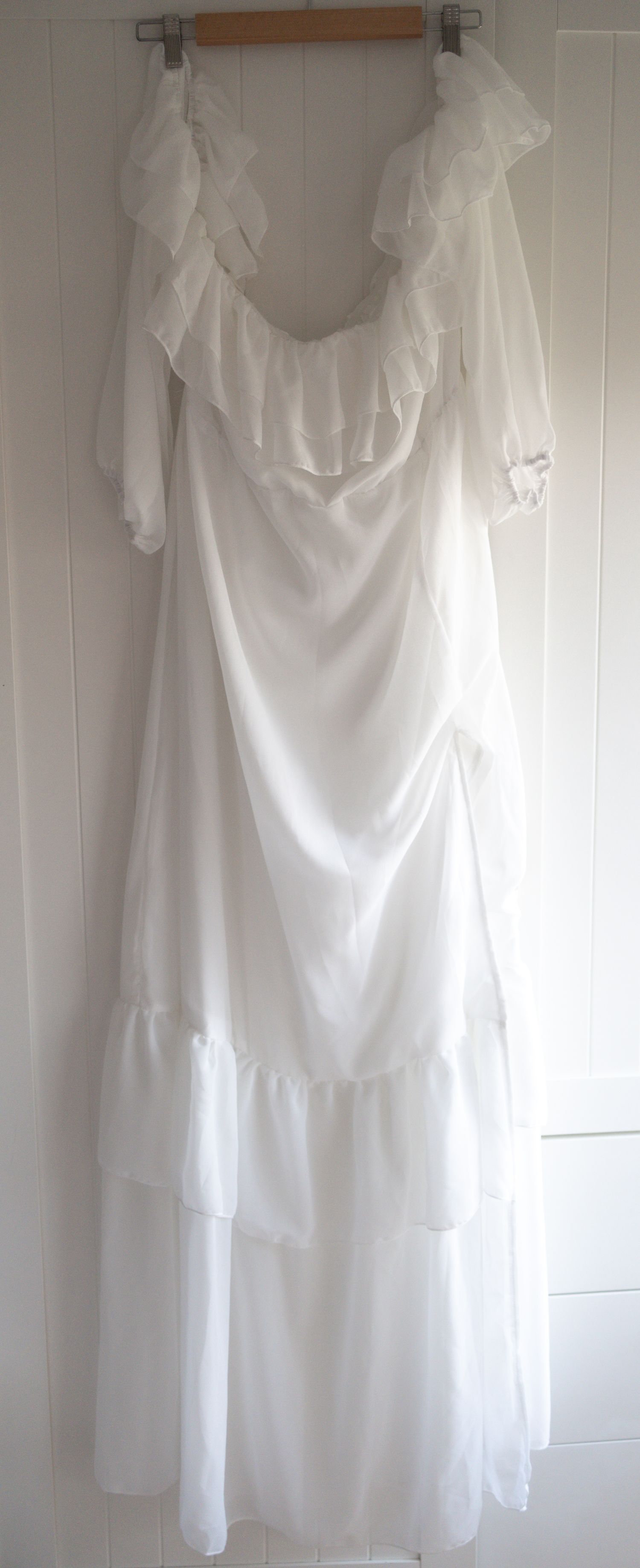 White vintage wedding dress with ruffled neckline, tiered skirt, and sheer sleeves hanging on wooden hanger.