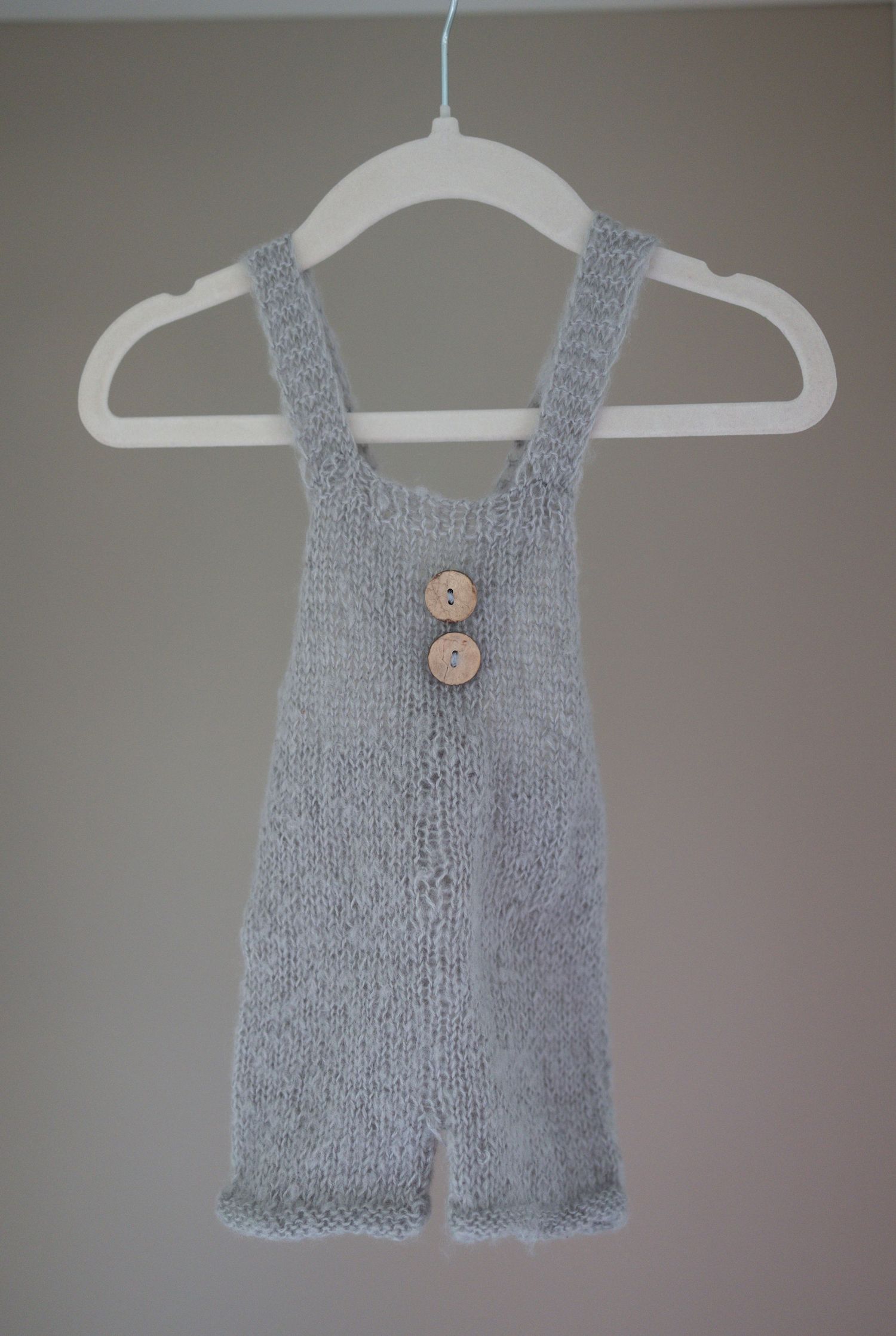 Hand-knitted gray baby romper with wooden buttons, displayed on a white hanger against a neutral wall. Taken by Golden Hour Perth