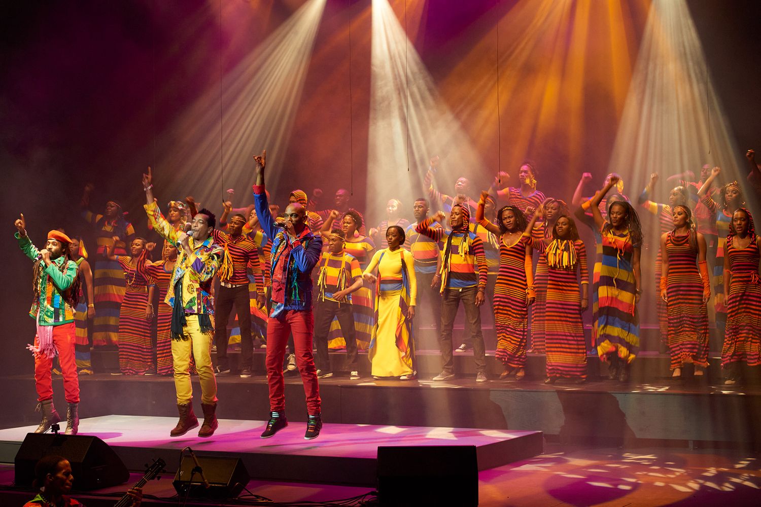 Colorful stage performance with performers in vibrant costumes under dramatic spotlights.