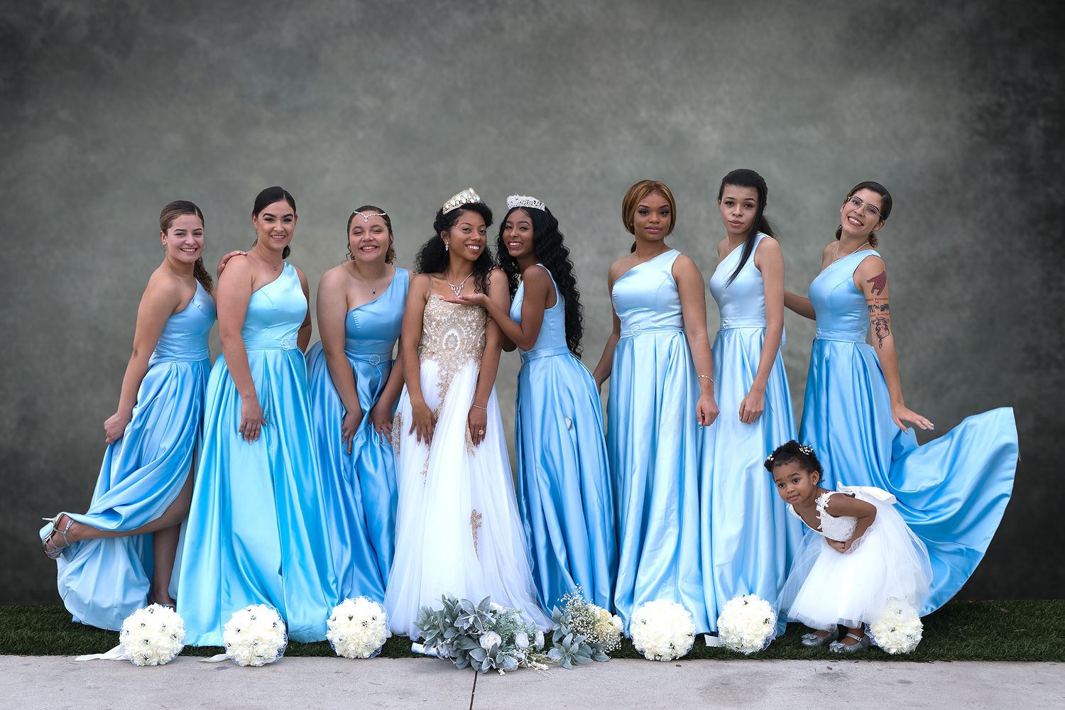 Bridal party in light blue gowns with bride in white posing together for a wedding photo.