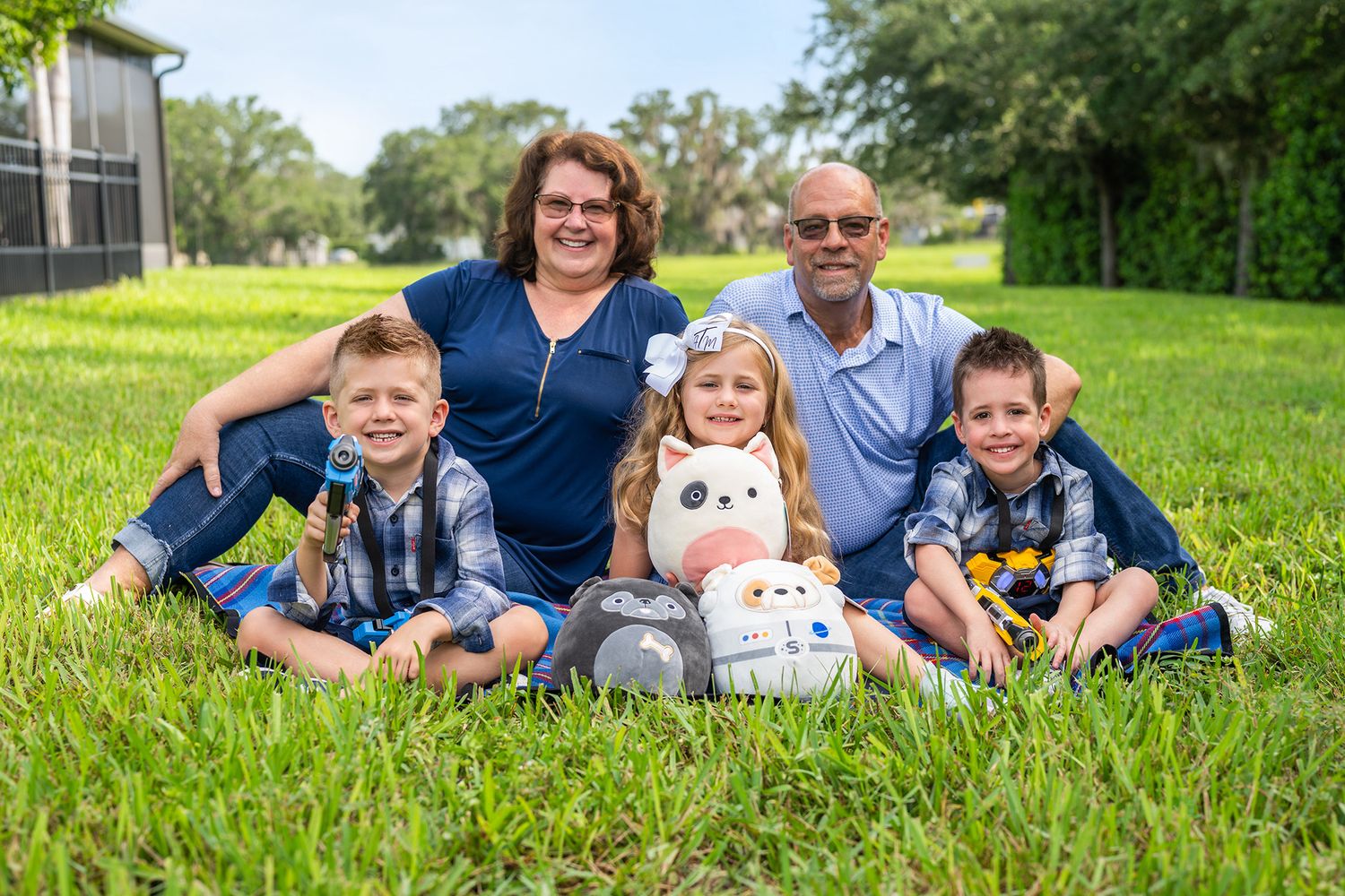 Family of grandparents and three young children smiling together on green lawn.