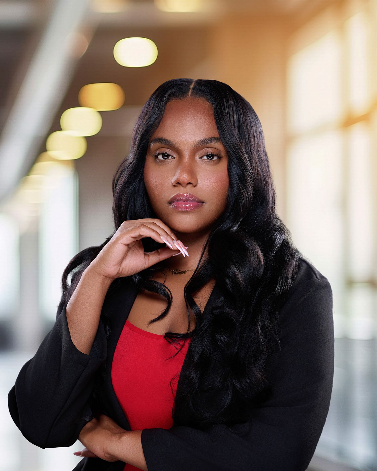 Confident young woman in red top and black blazer poses in modern well-lit professional setting.