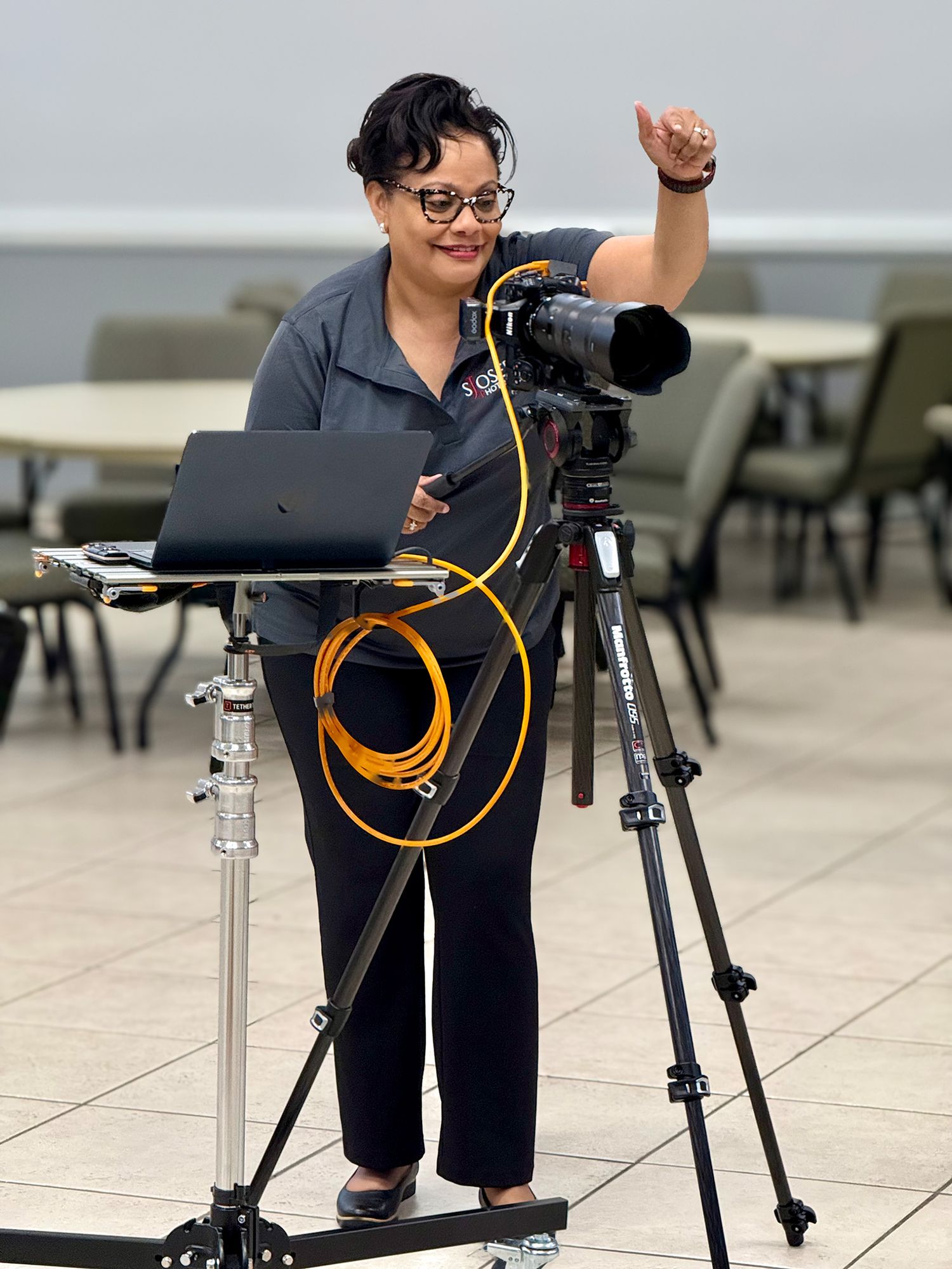 Solange Joseph, photographer giving thumbs up while operating professional camera on tripod at event.