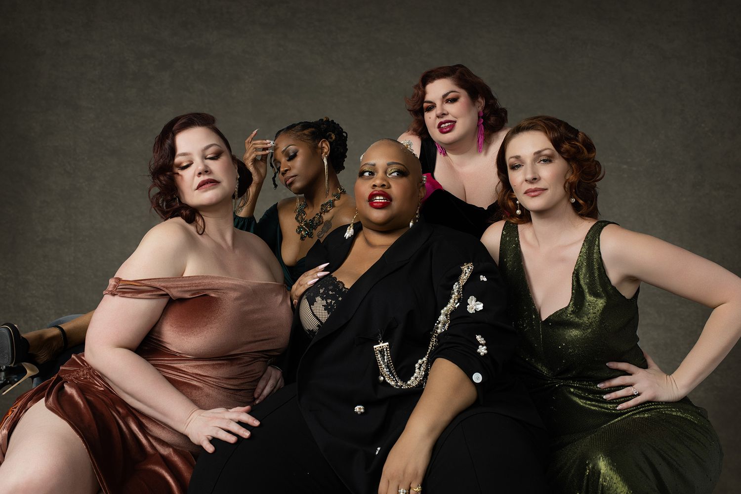 Five diverse plus-size women pose elegantly in colorful formal gowns for a glamorous studio fashion shoot.