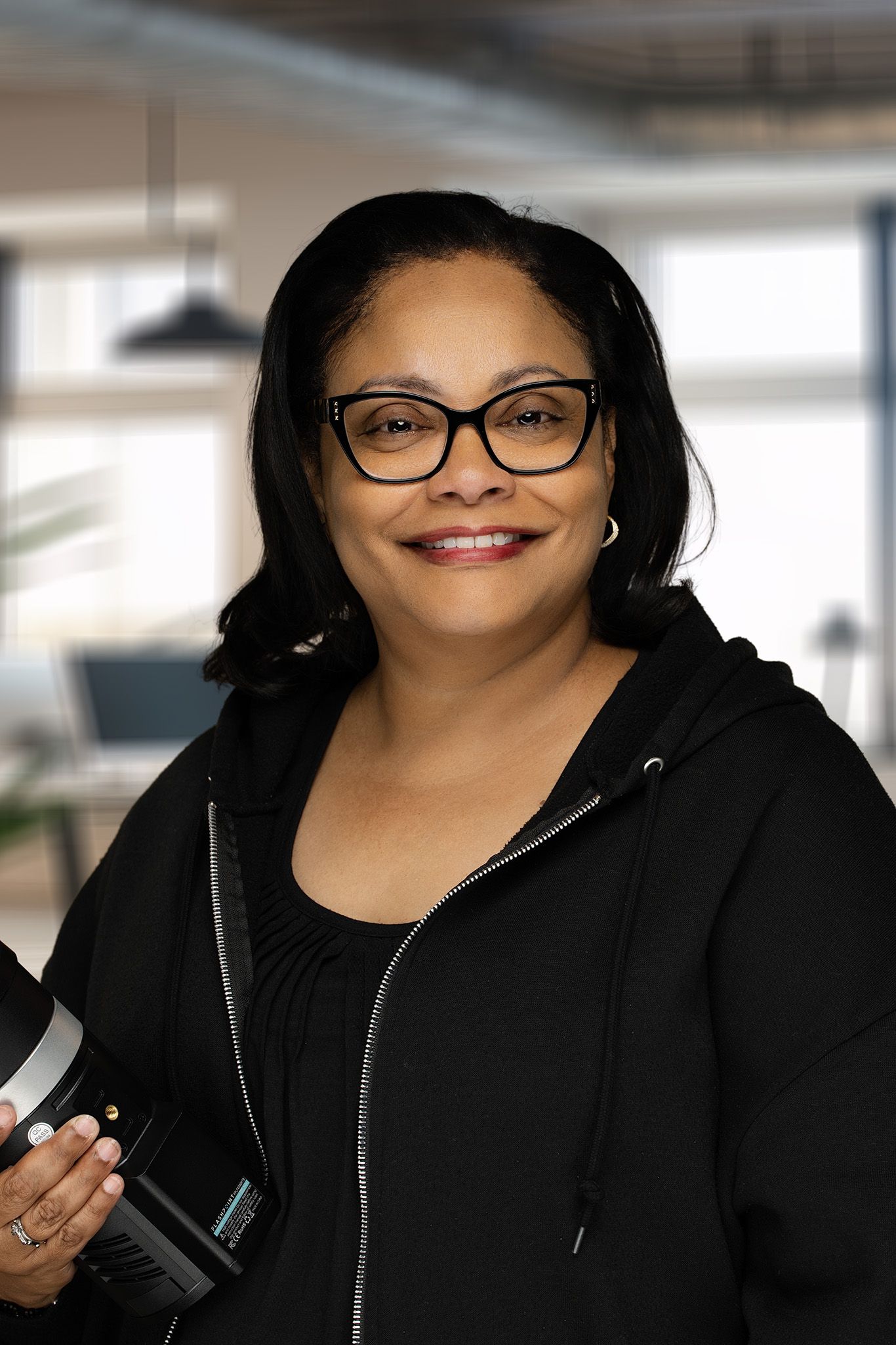 Solange Joseph, photographer, smiling while holding monolight in modern office.