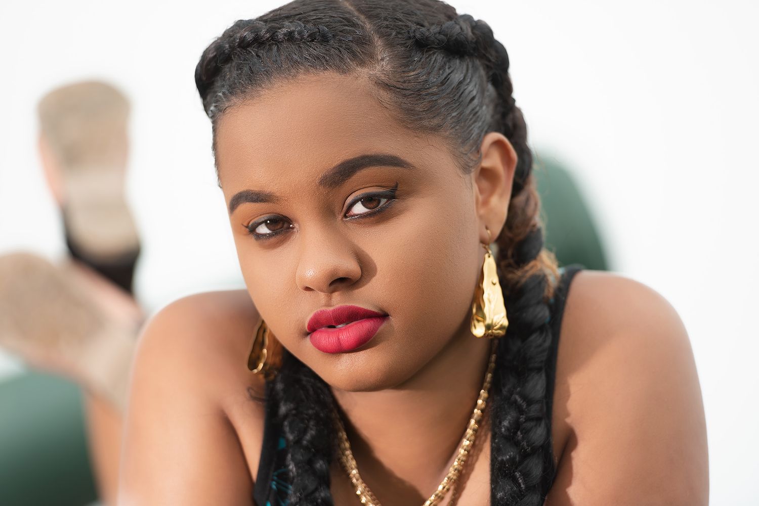 A young woman with braided hair and gold jewelry poses with bold red lips in a fashion portrait.