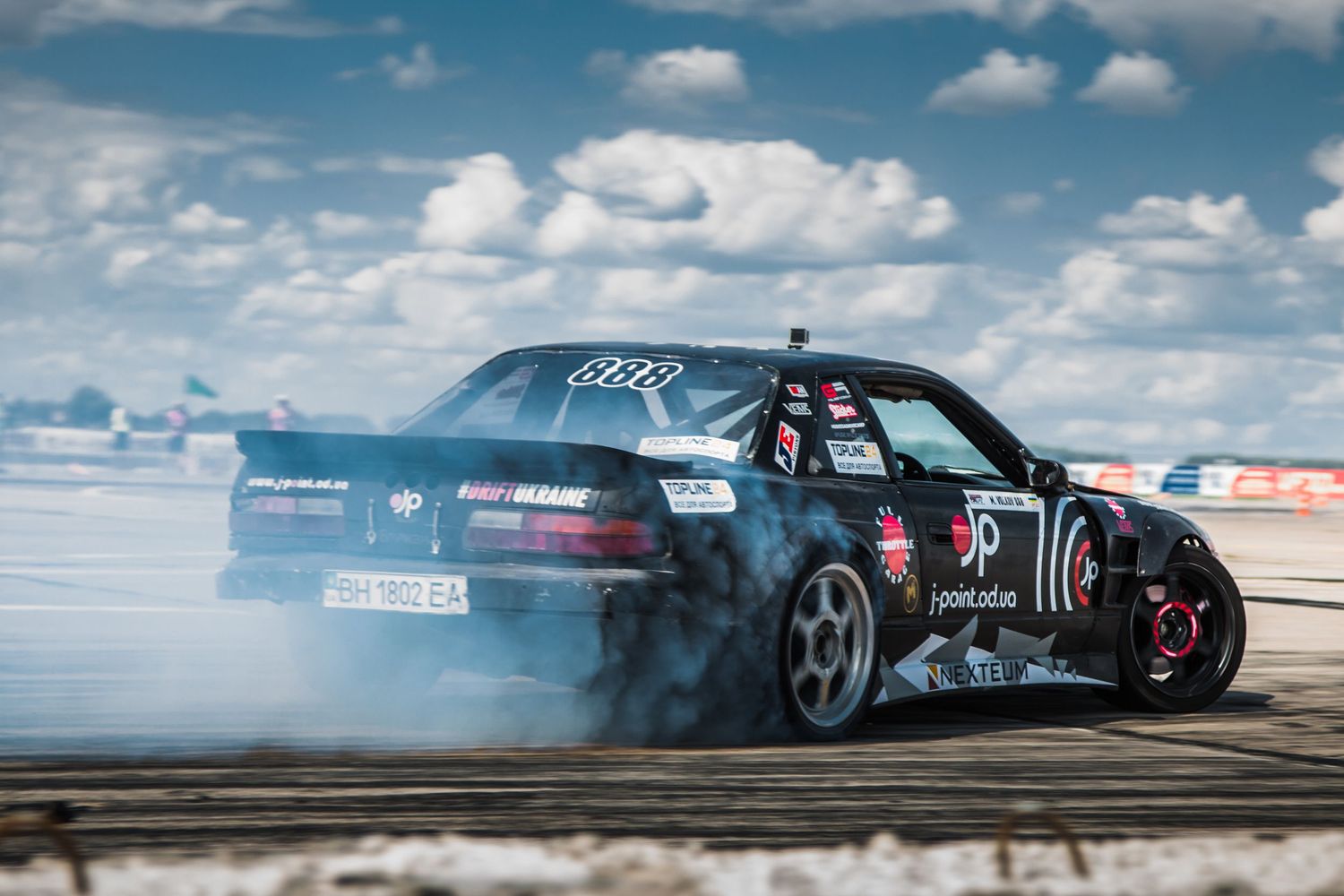 Drift car performing a burnout on a racetrack under a blue sky.