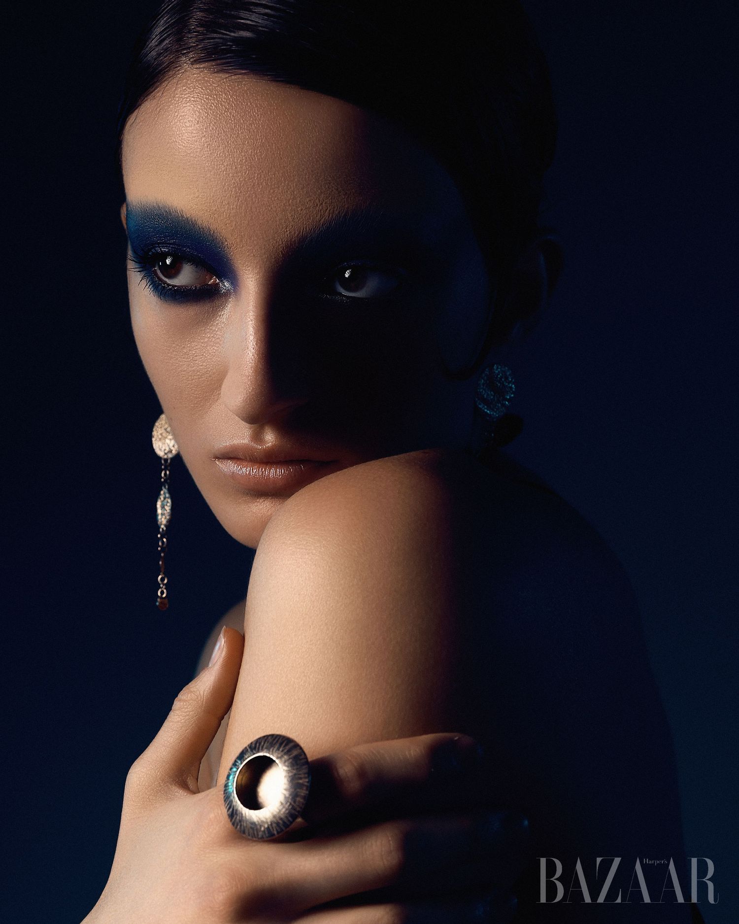 Editorial beauty portrait of a female model with dramatic blue eye makeup and cinematic lighting.