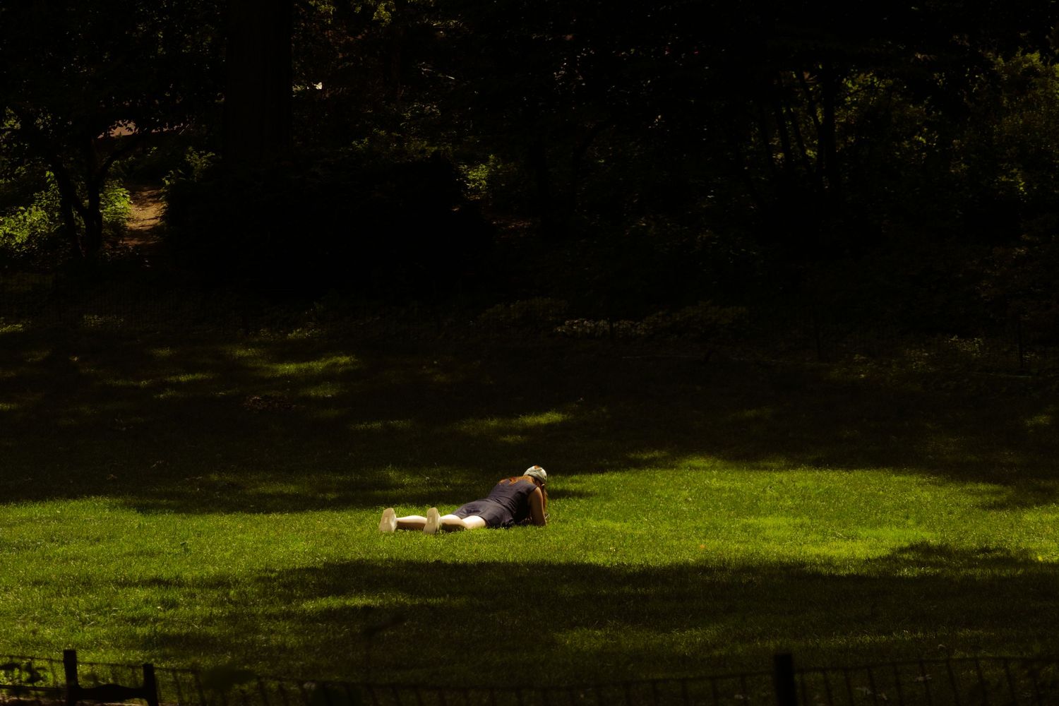 Street style portrait of a woman relaxing on a grassy field in a New York City park.