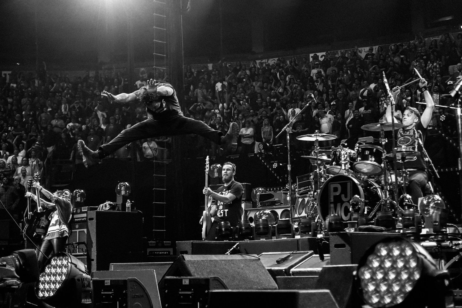 Black and white photo of Eddie Vedder jumping high in the air during a Pearl Jam concert, photographed by concert photographer Lisa Mark.