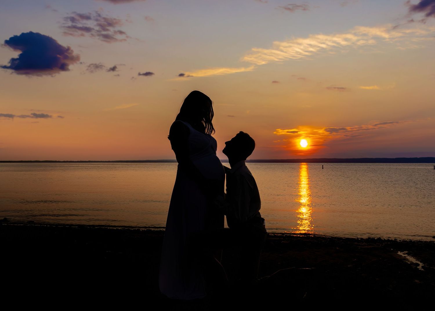 Silhouette of a pregnant couple sharing a tender moment on the beach during a golden sunset.