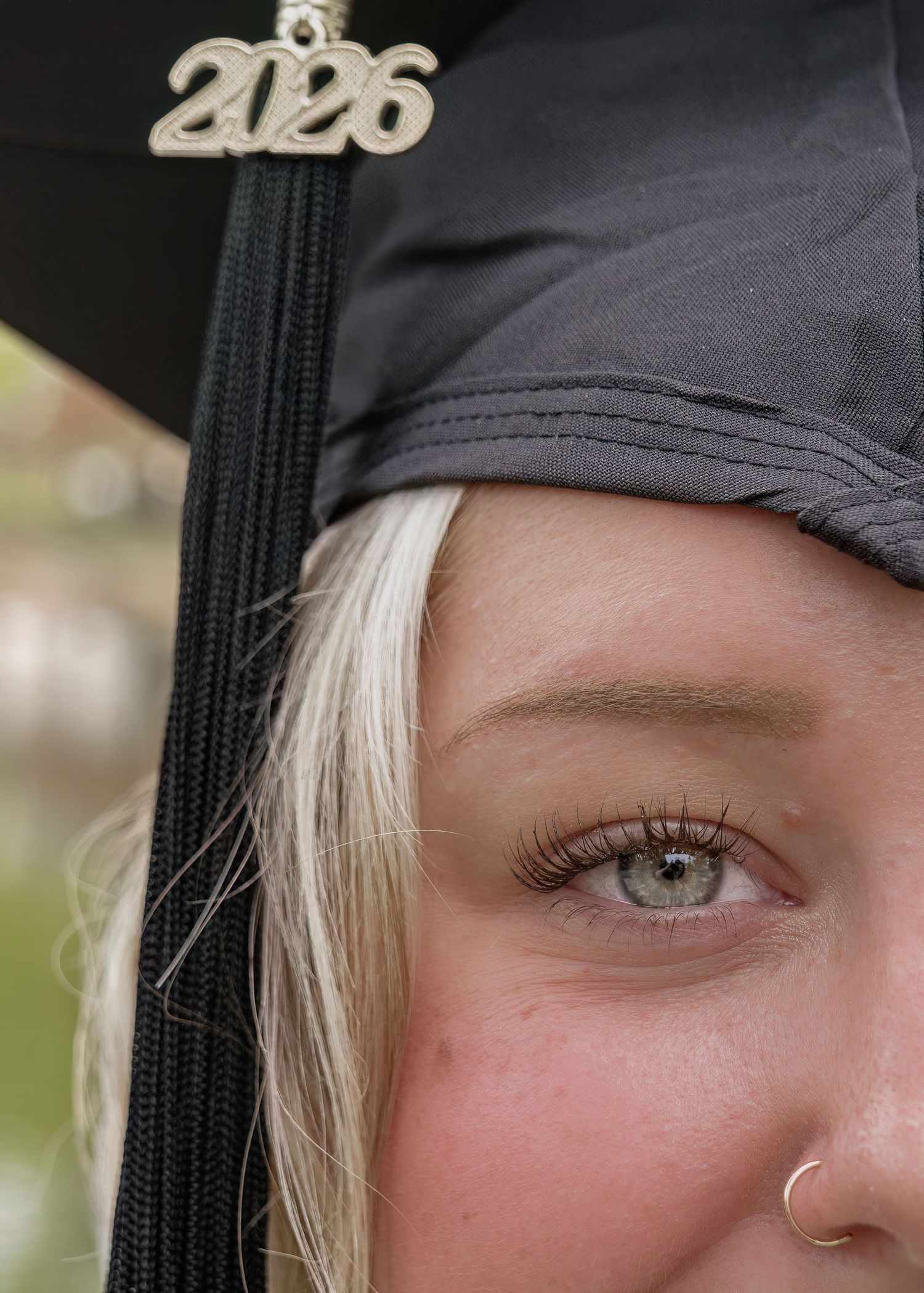 Close-up of a blue-eyed graduate wearing a black cap with a 2026 tassel charm and a nose ring.
