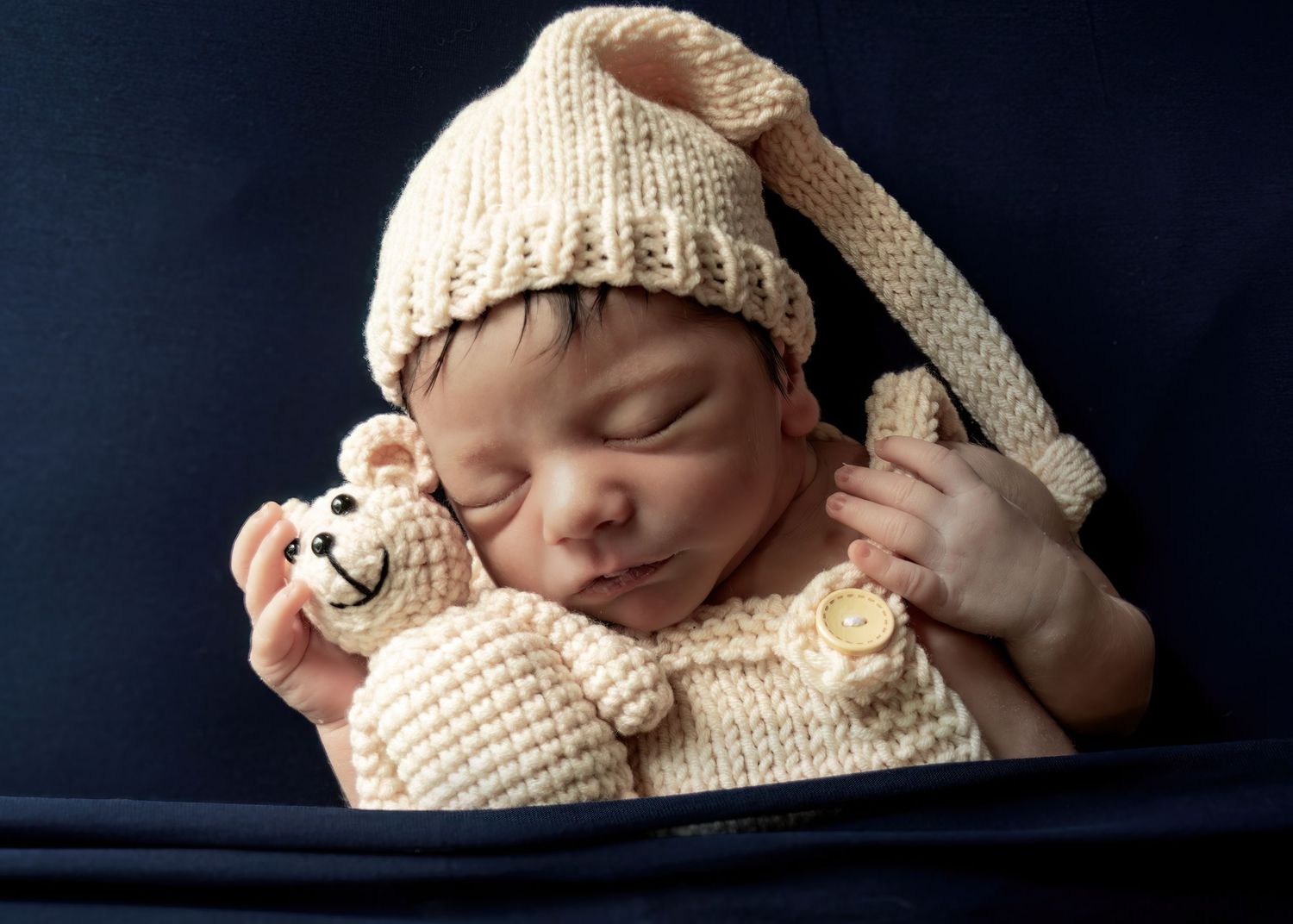 Sleeping newborn wearing cream knit bunny hat and outfit holding matching teddy bear.