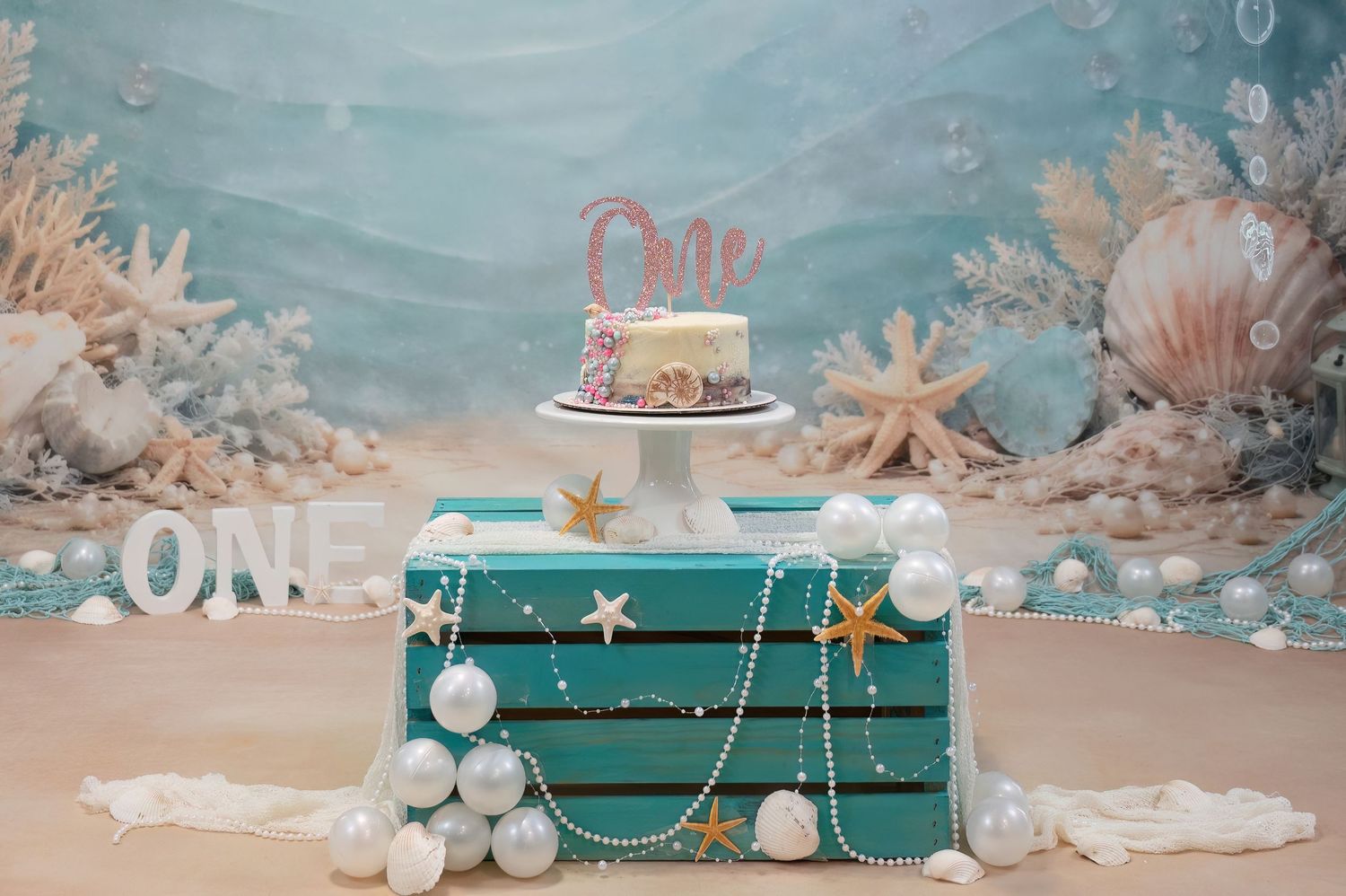 Ocean-themed first birthday cake display with starfish and pearl decorations.